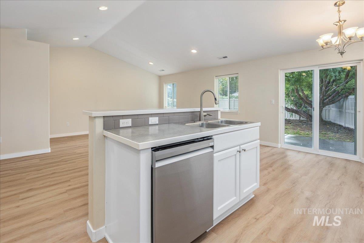 Kitchen featuring an island with sink, stainless steel dishwasher, lofted ceiling, white cabinetry, and light countertops