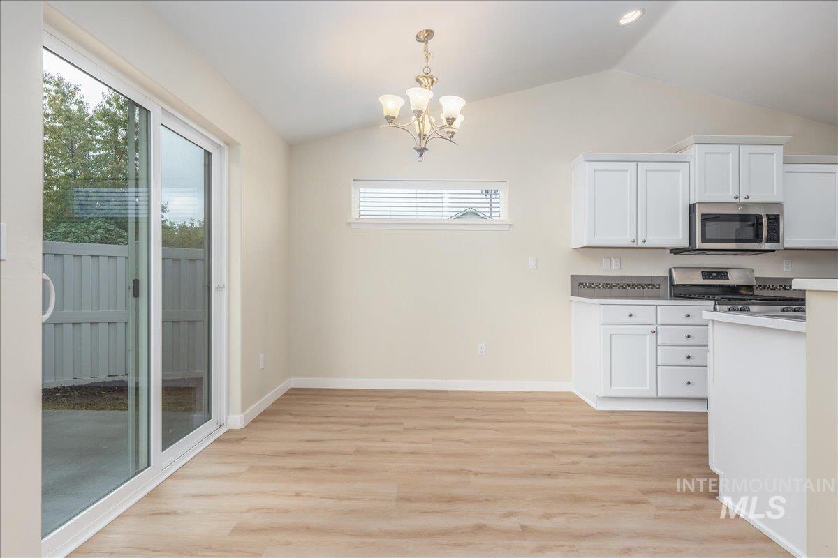 Kitchen featuring white cabinets, lofted ceiling, decorative light fixtures, light countertops, and light wood-style flooring