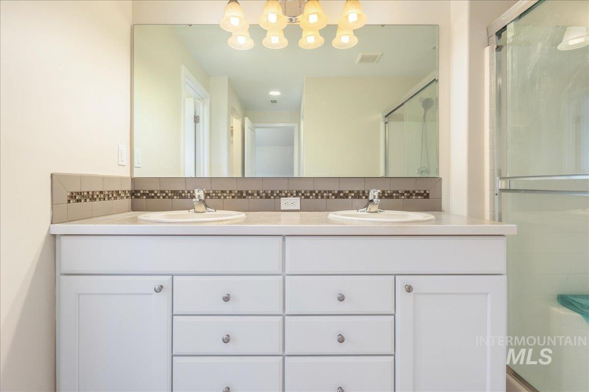 Full bath with double vanity, a shower stall, and decorative backsplash