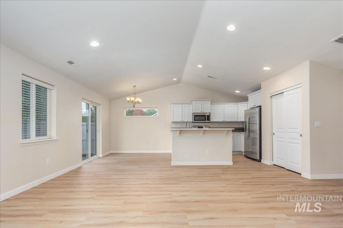Kitchen featuring lofted ceiling, a chandelier, a breakfast bar, white cabinets, and stainless steel appliances