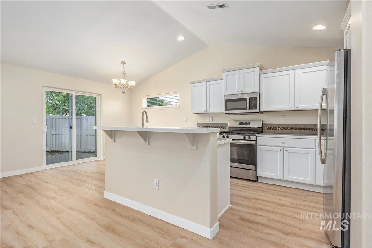 Kitchen featuring appliances with stainless steel finishes, a kitchen bar, white cabinetry, a kitchen island with sink, and lofted ceiling