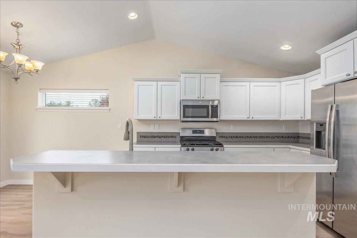 Kitchen with a breakfast bar area, appliances with stainless steel finishes, a center island, white cabinets, and vaulted ceiling
