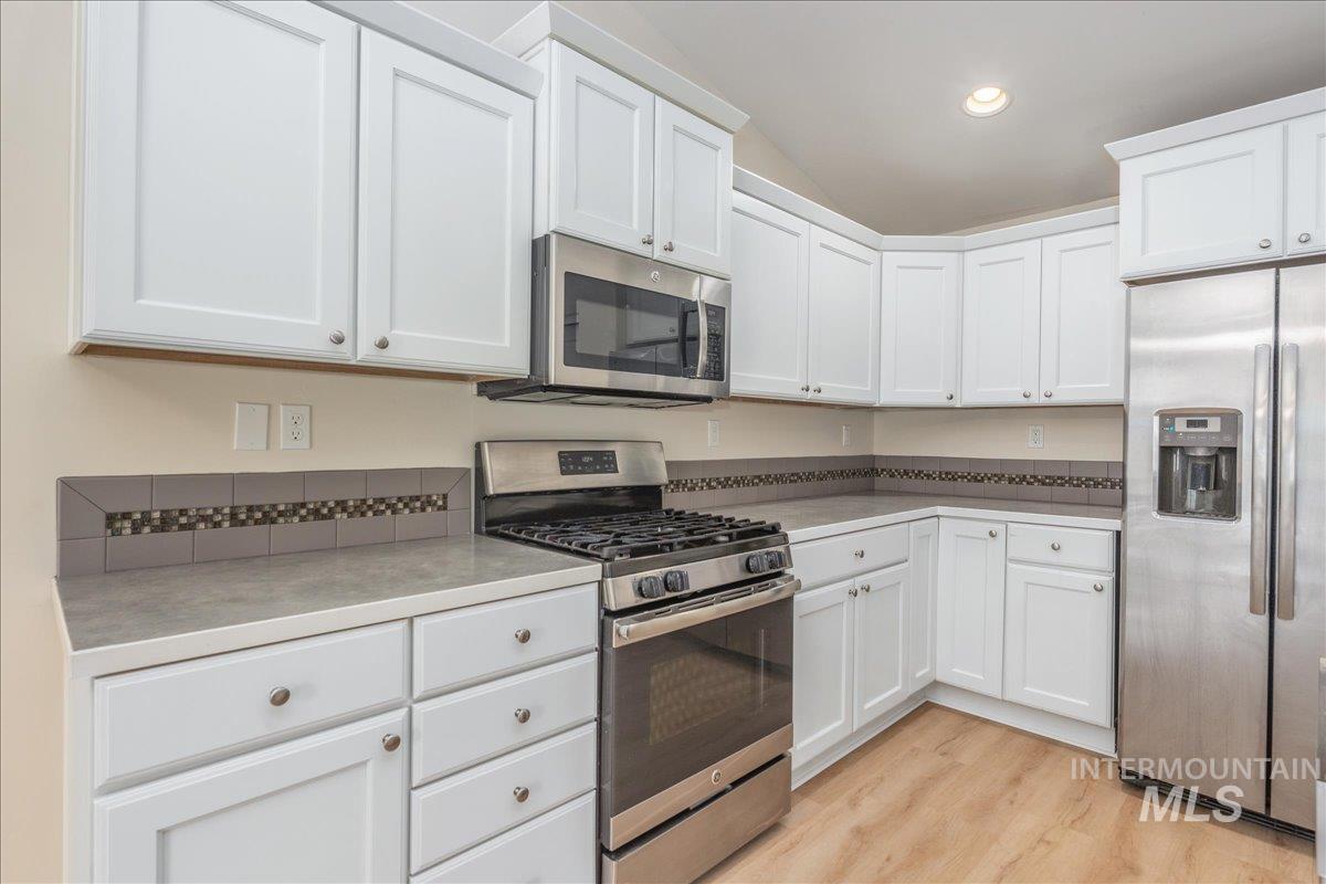 Kitchen with stainless steel appliances, white cabinets, light wood-style floors, recessed lighting, and vaulted ceiling