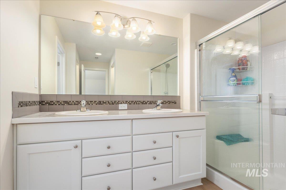 Full bath with double vanity, a shower stall, and backsplash