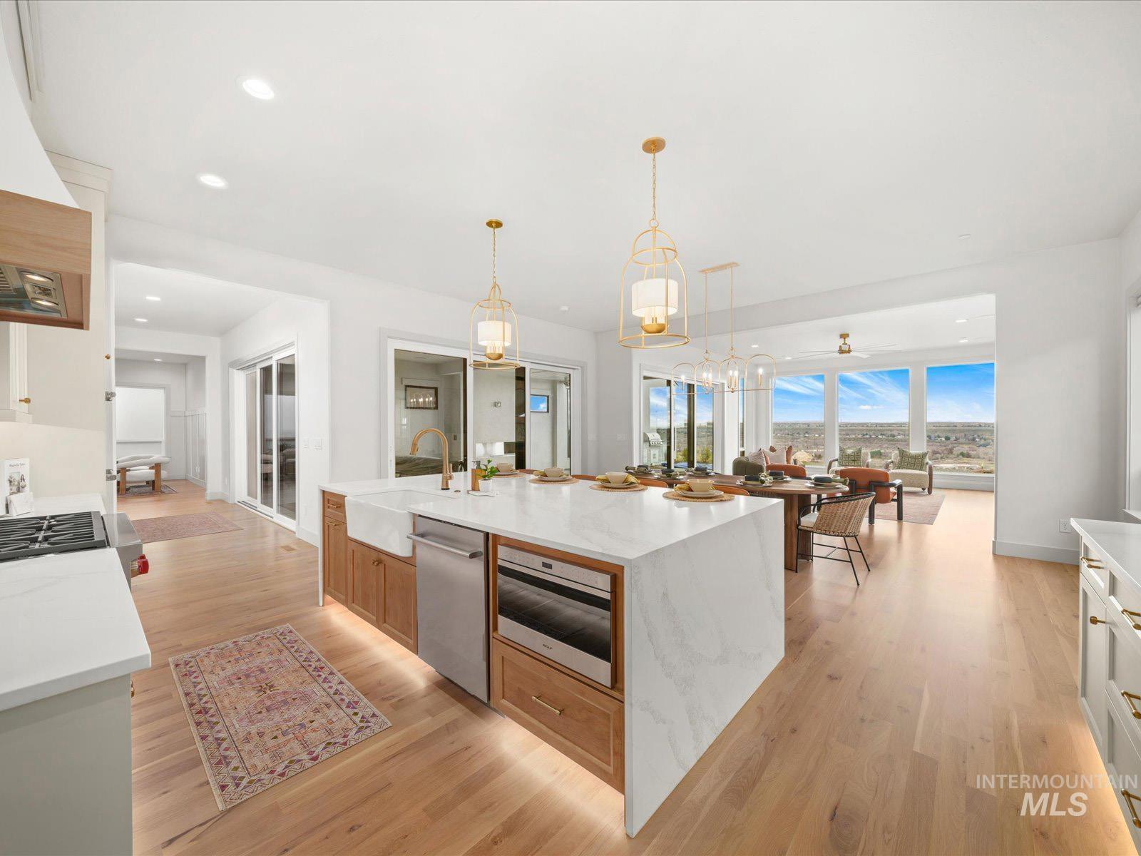 Kitchen with light stone counters, light wood finished floors, stainless steel appliances, a center island with sink, and dual tone cabinets