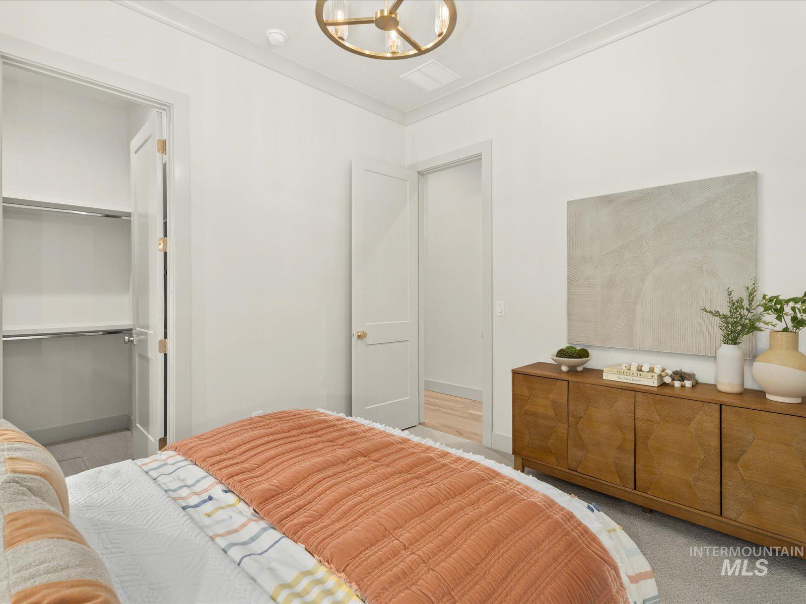 Bedroom with hanging lights, light colored carpet, a spacious closet, and crown molding