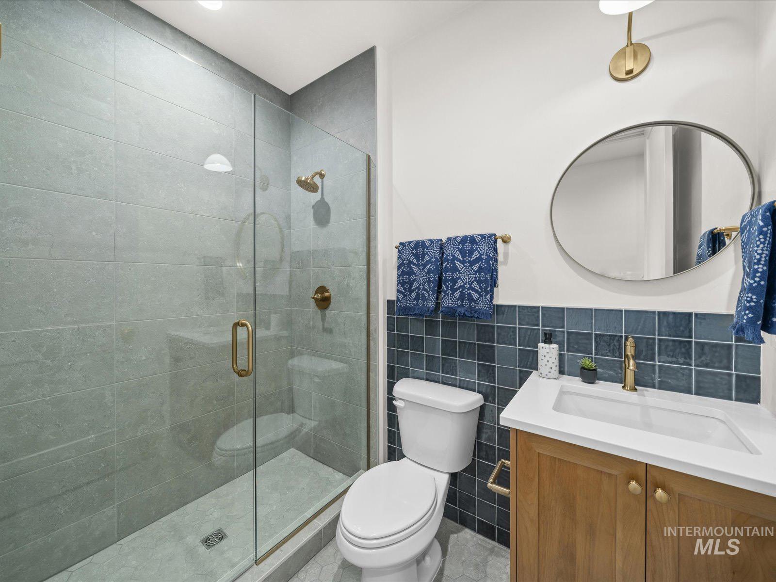 Bathroom featuring vanity, tile walls, a shower stall, and a wainscoted wall