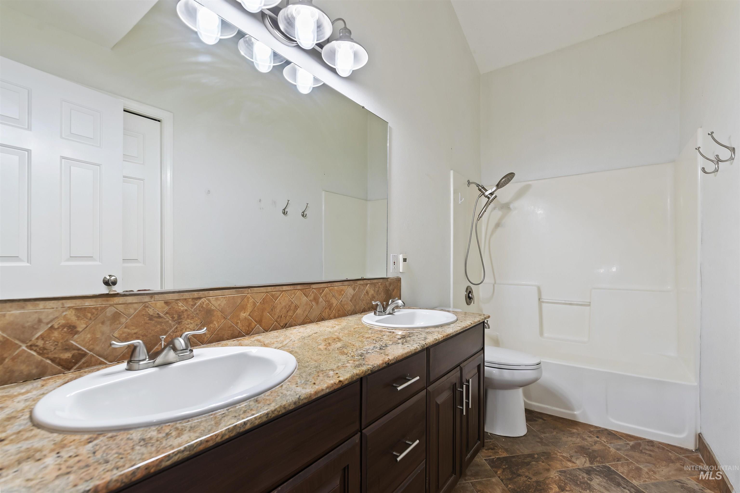 Full bathroom featuring double vanity, shower / washtub combination, backsplash, and stone finish floors