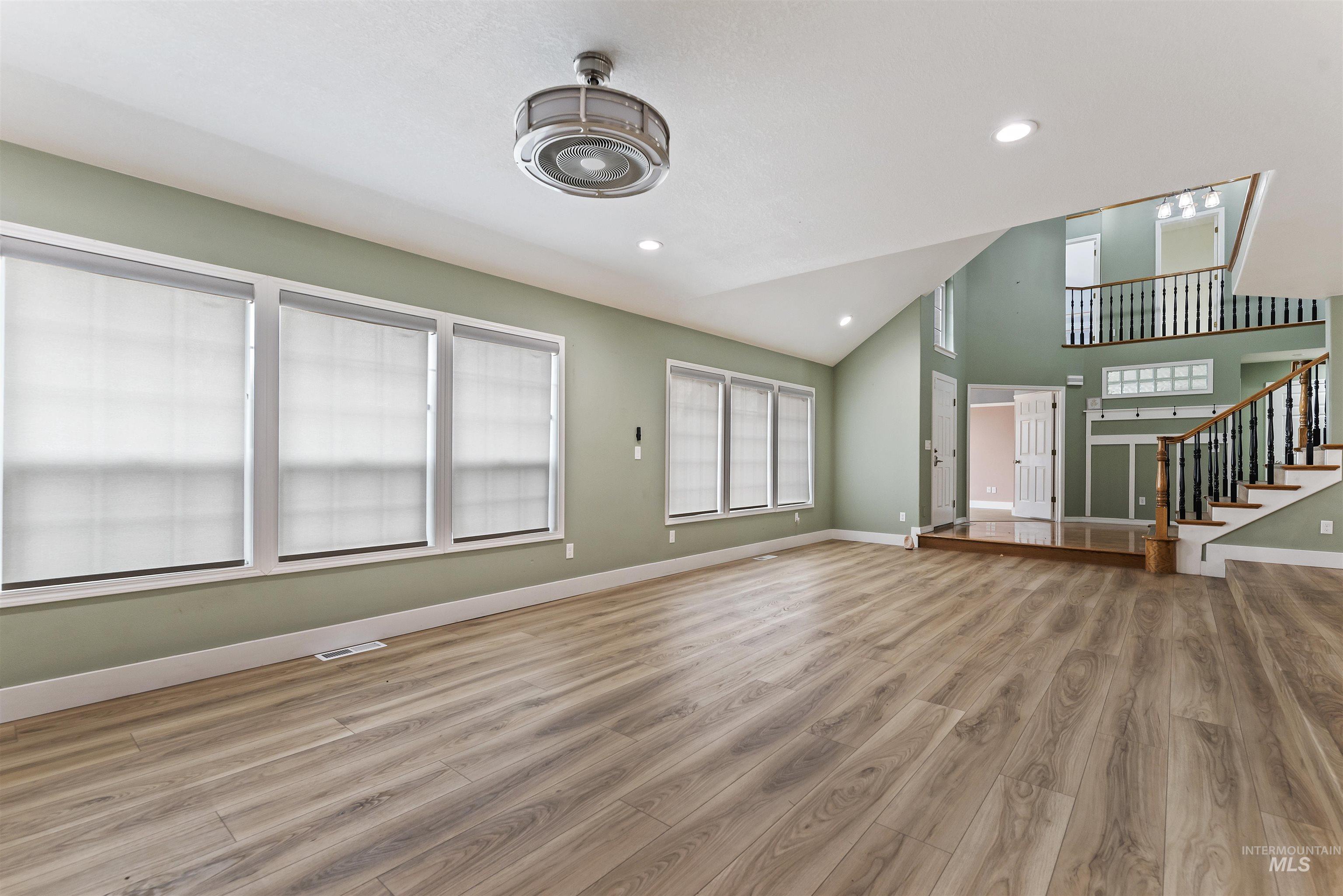 Unfurnished living room featuring stairs, light wood-type flooring, recessed lighting, and high vaulted ceiling