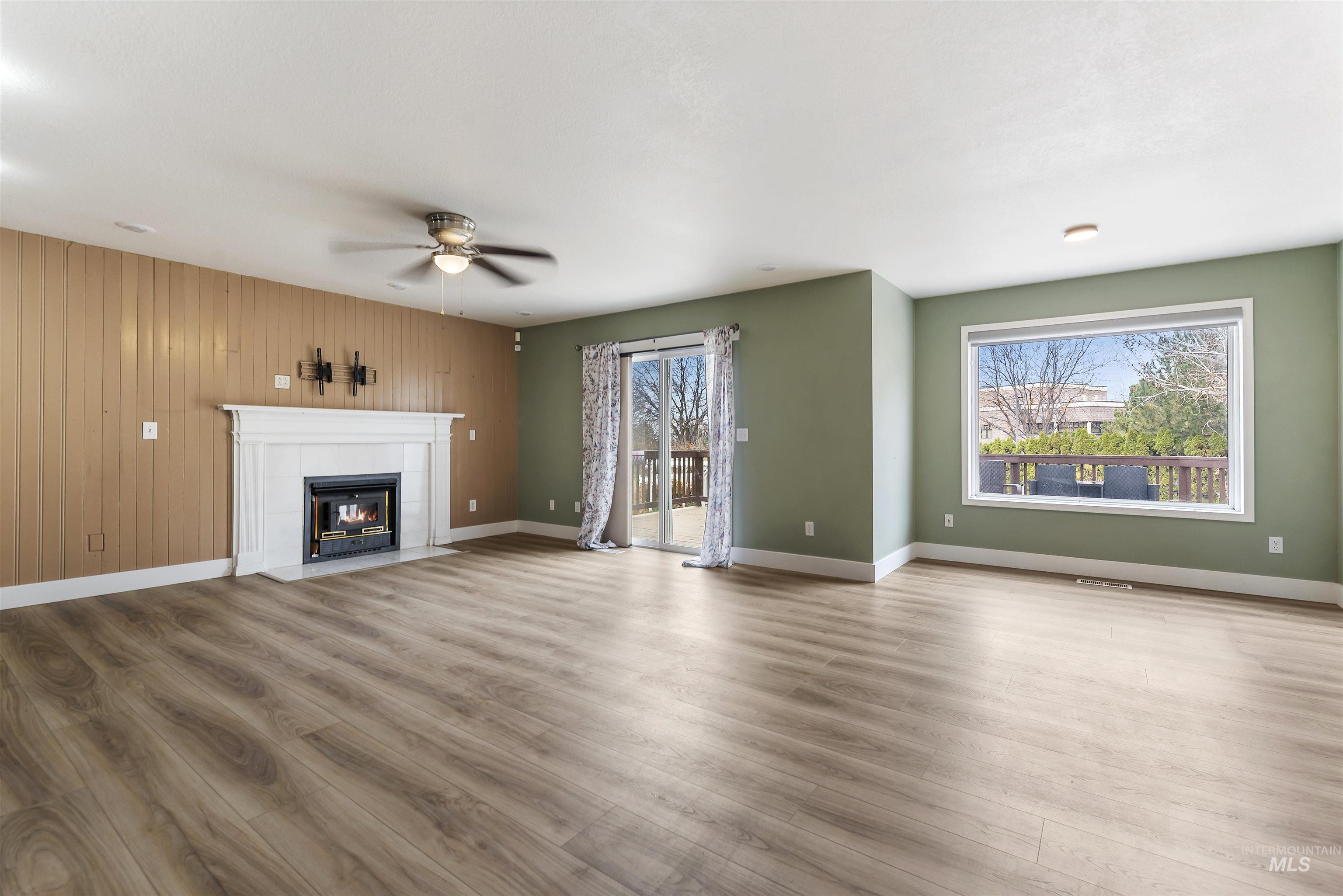 Unfurnished living room with a tiled fireplace, wood finished floors, wood walls, and a ceiling fan