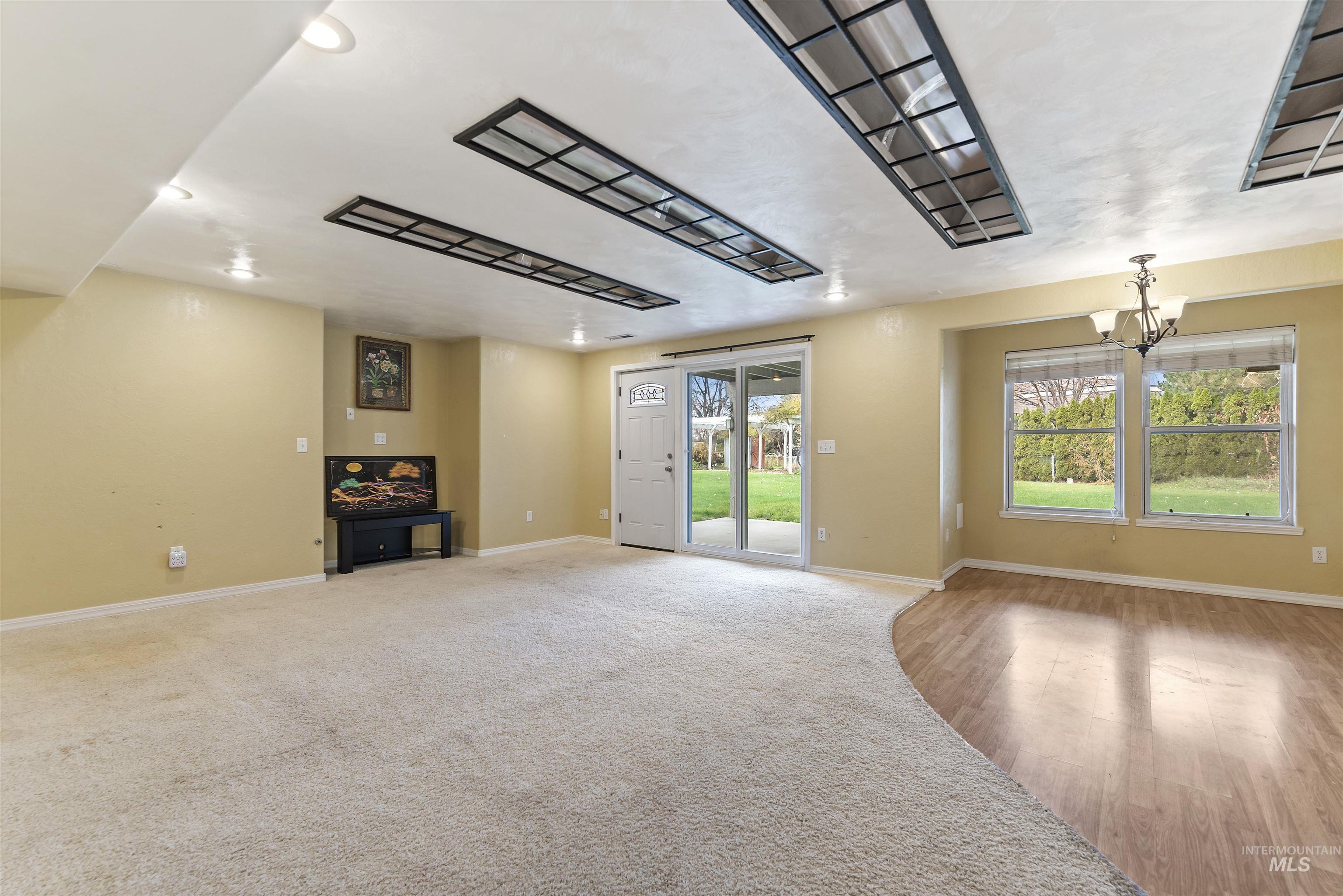 Unfurnished living room featuring baseboards and a chandelier