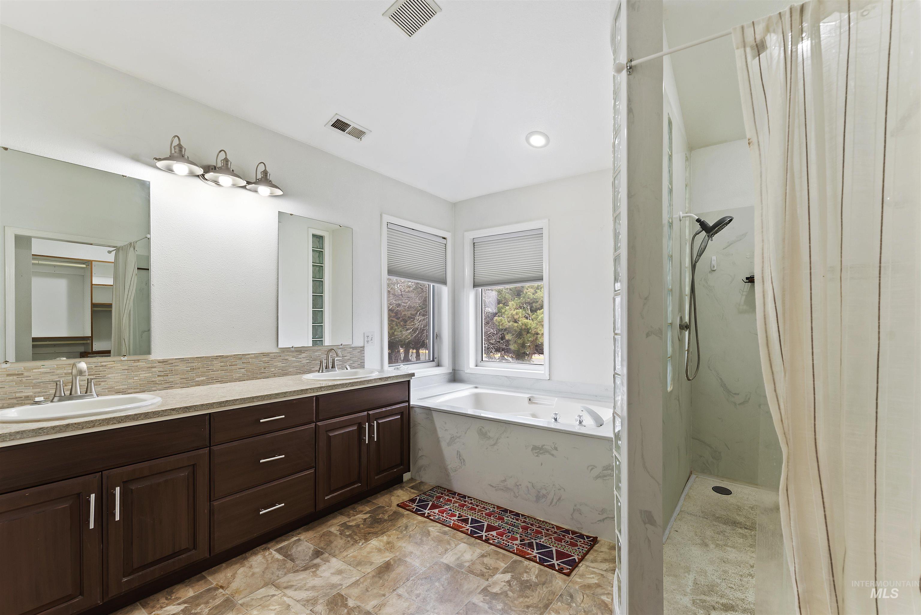 Full bathroom with a marble finish shower, double vanity, a bath, decorative backsplash, and stone finish floors