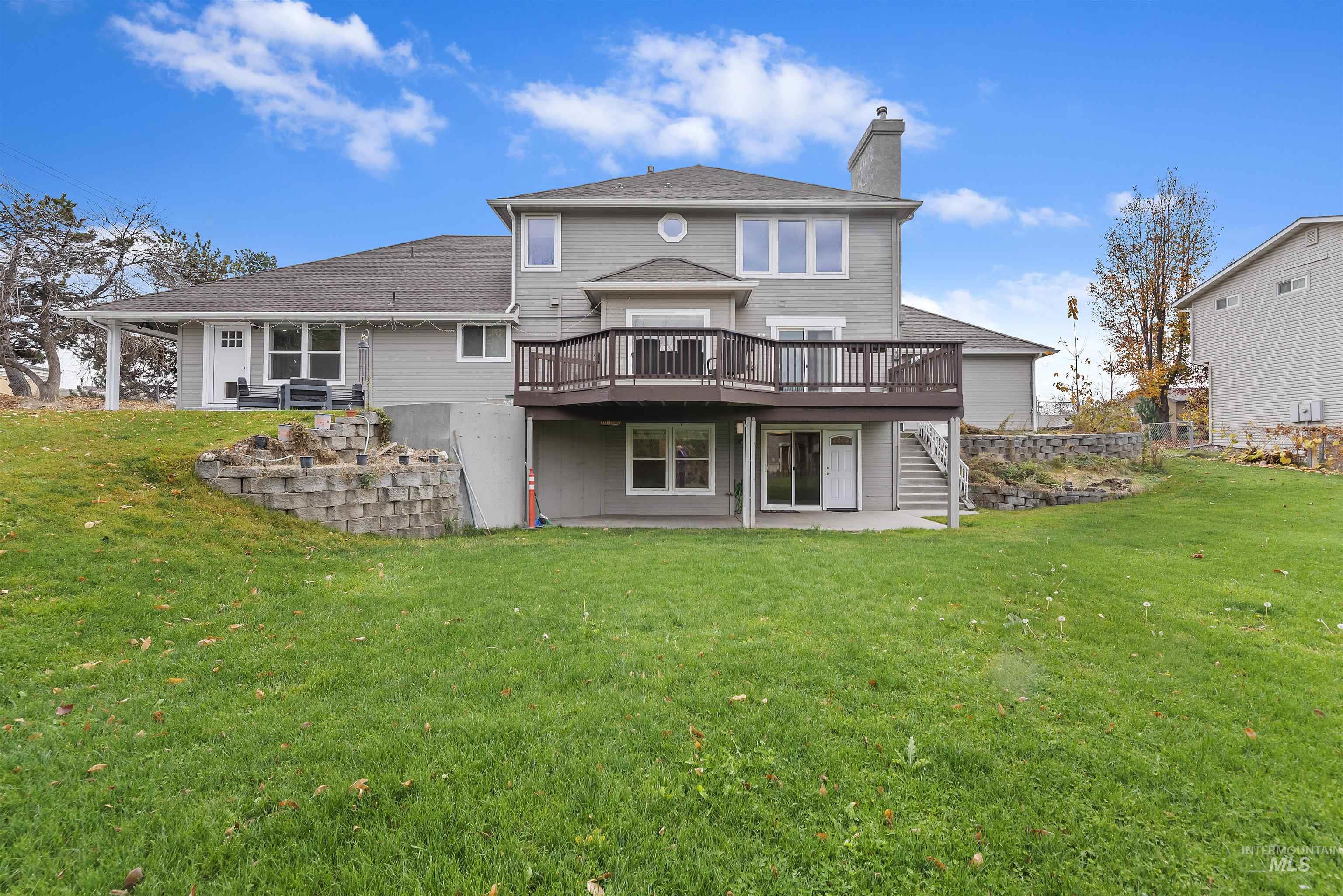Back of house with a wooden deck, a patio area, a lawn, and a chimney