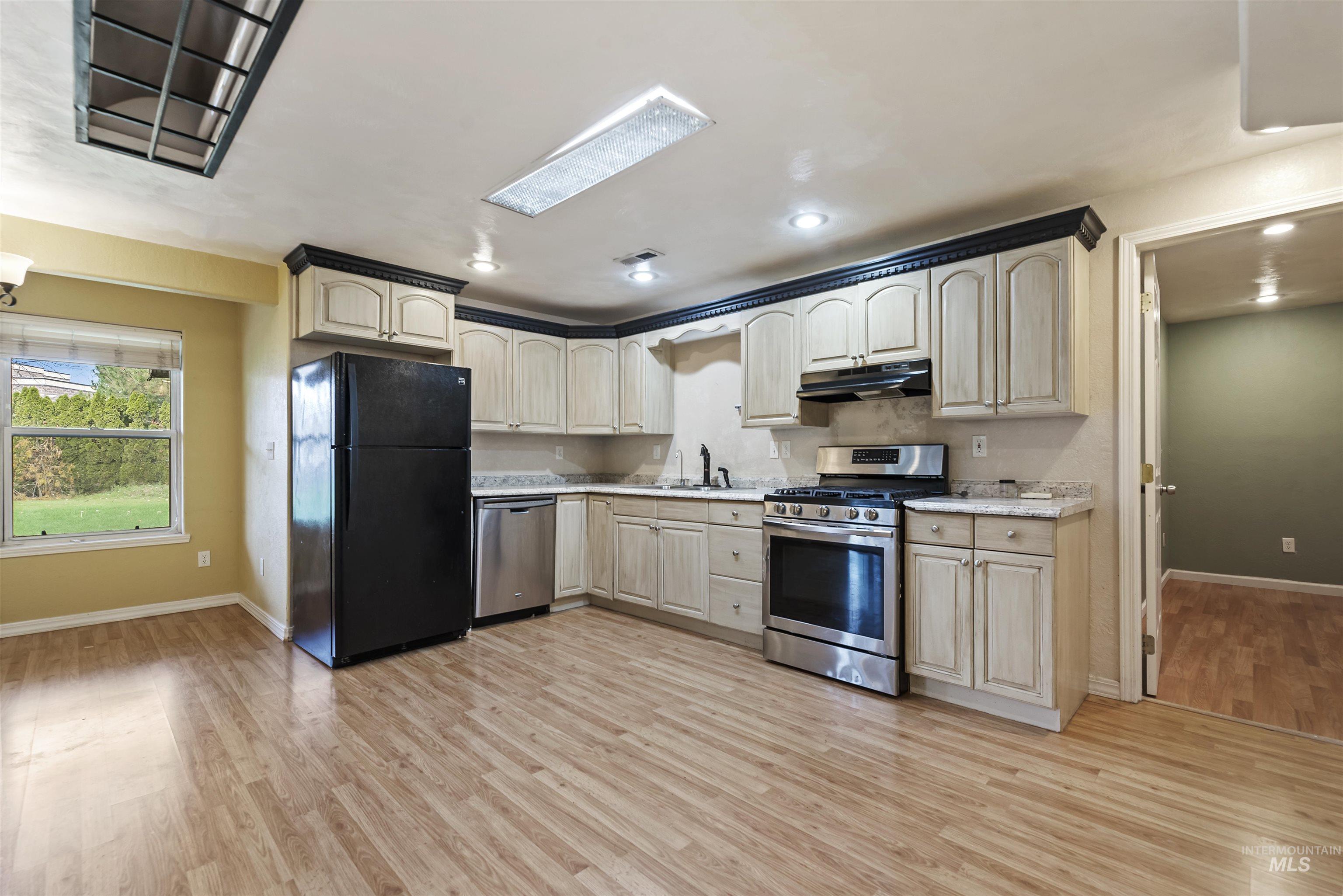 Kitchen with appliances with stainless steel finishes, light countertops, light wood-style flooring, under cabinet range hood, and recessed lighting