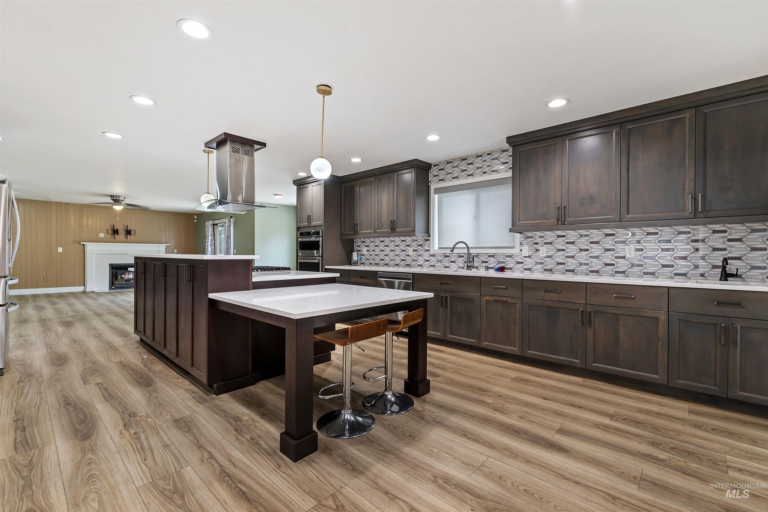 Kitchen with dark brown cabinets, a fireplace, tasteful backsplash, hanging light fixtures, and a center island