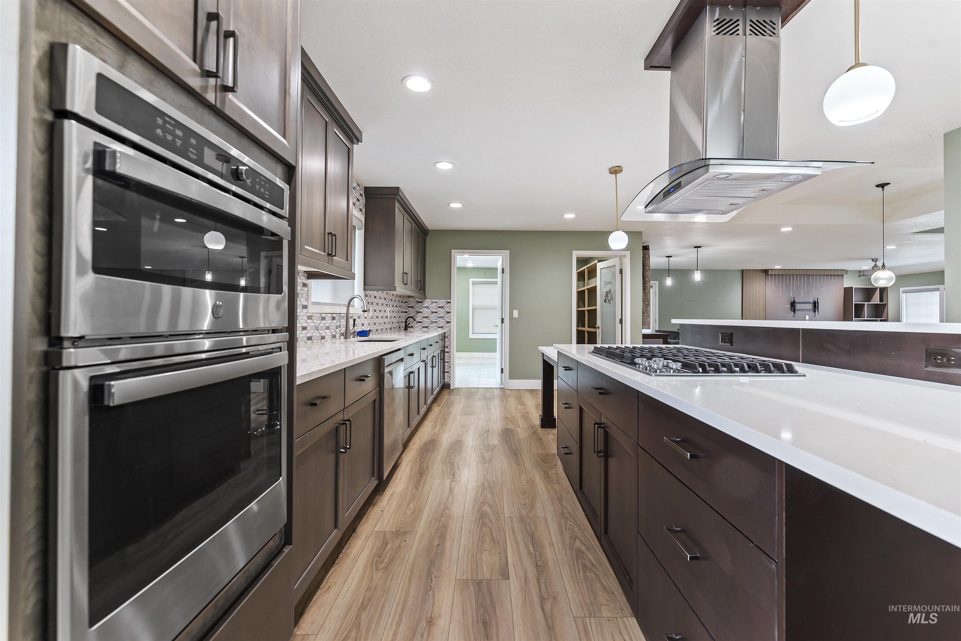 Kitchen featuring appliances with stainless steel finishes, island range hood, dark brown cabinets, decorative light fixtures, and recessed lighting