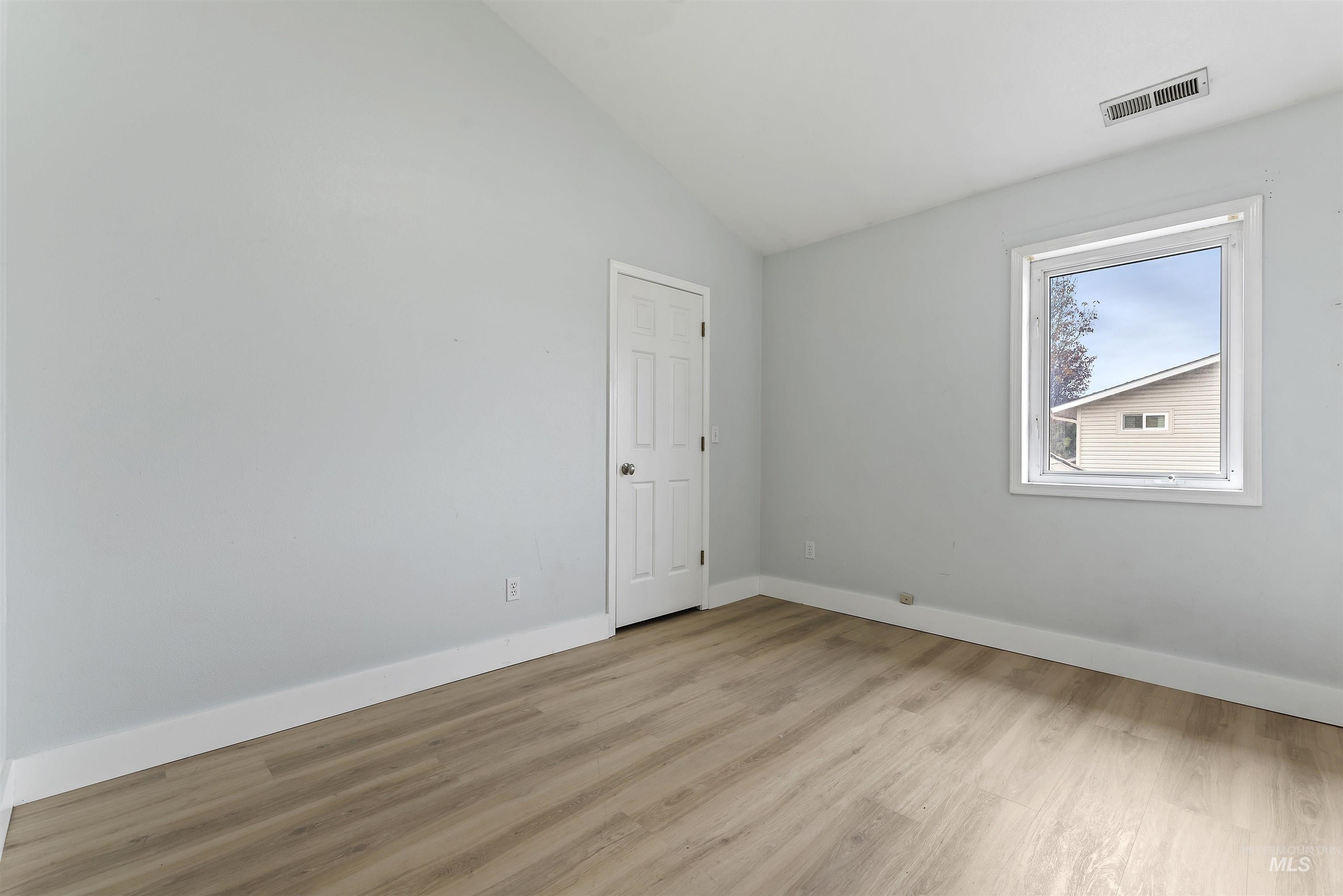 Empty room with vaulted ceiling and light wood-style floors