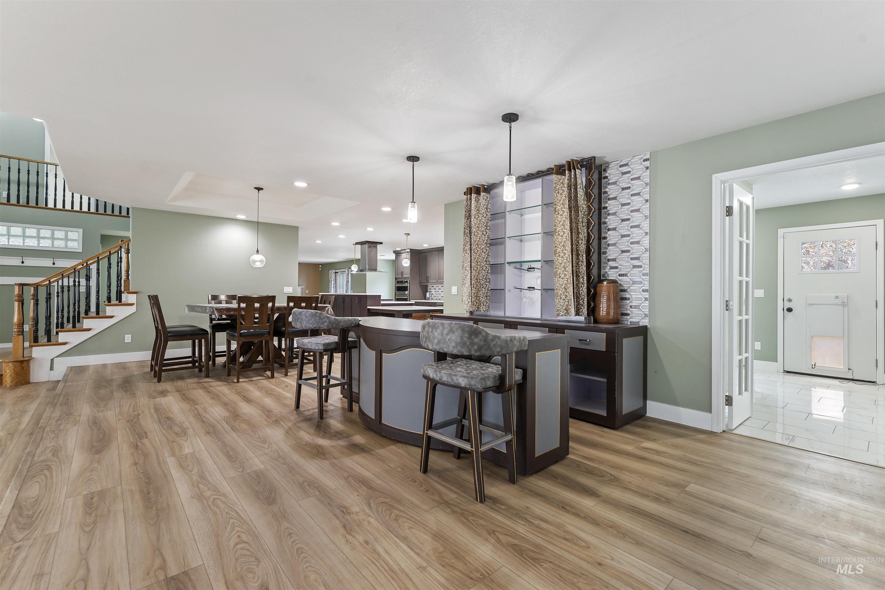 Bar area featuring dark countertops, hanging light fixtures, a tray ceiling, stairway, and light wood-type flooring