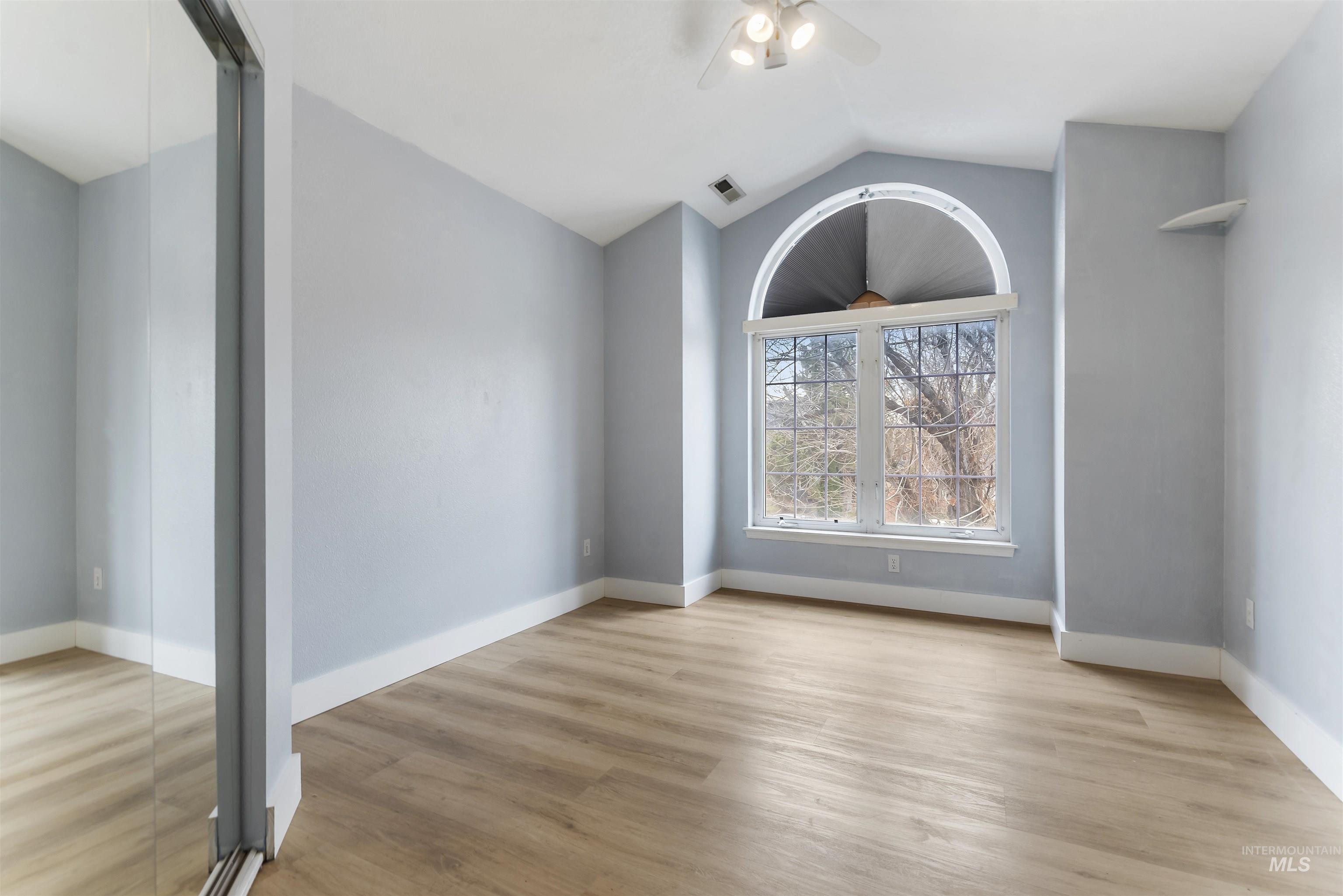 Empty room featuring vaulted ceiling, light wood finished floors, and ceiling fan