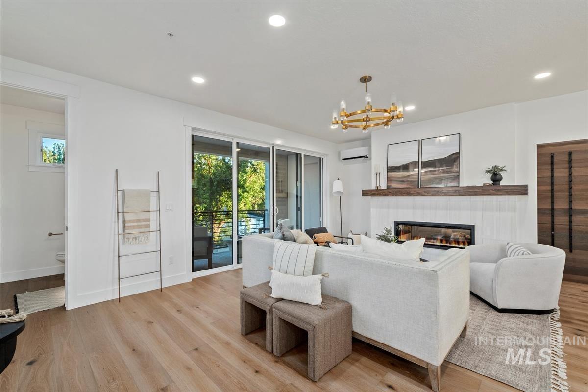 Living area featuring light wood finished floors, a tiled fireplace, recessed lighting, a chandelier, and a wall unit AC