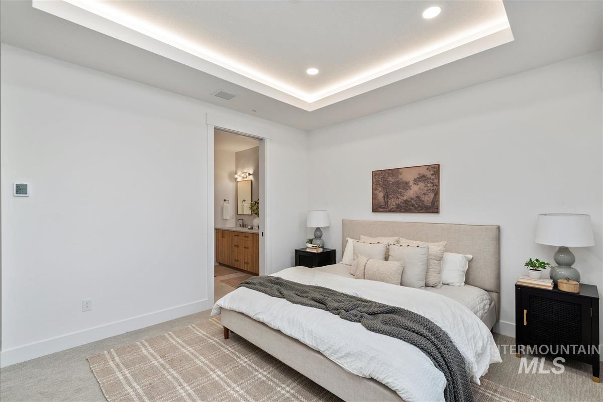 Carpeted bedroom featuring a raised ceiling, ensuite bath, and recessed lighting