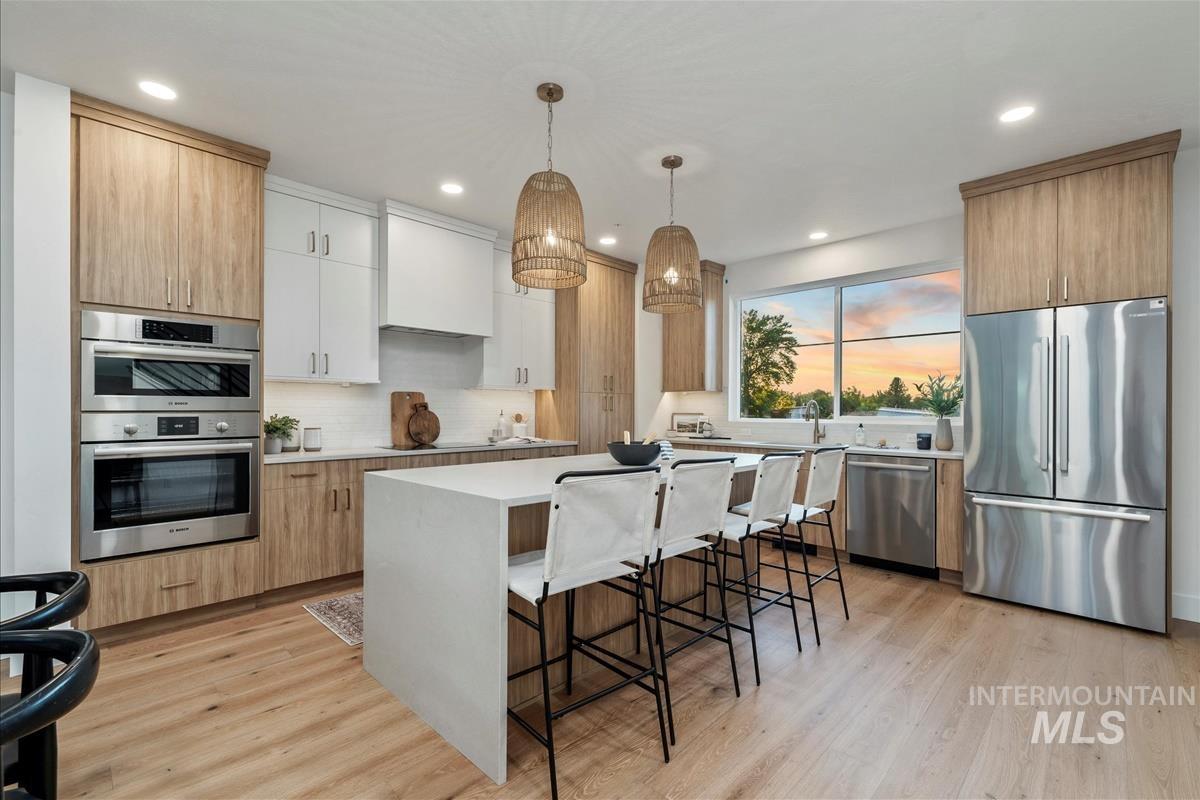 Kitchen featuring appliances with stainless steel finishes, a kitchen bar, light brown cabinets, decorative light fixtures, and light wood-type flooring