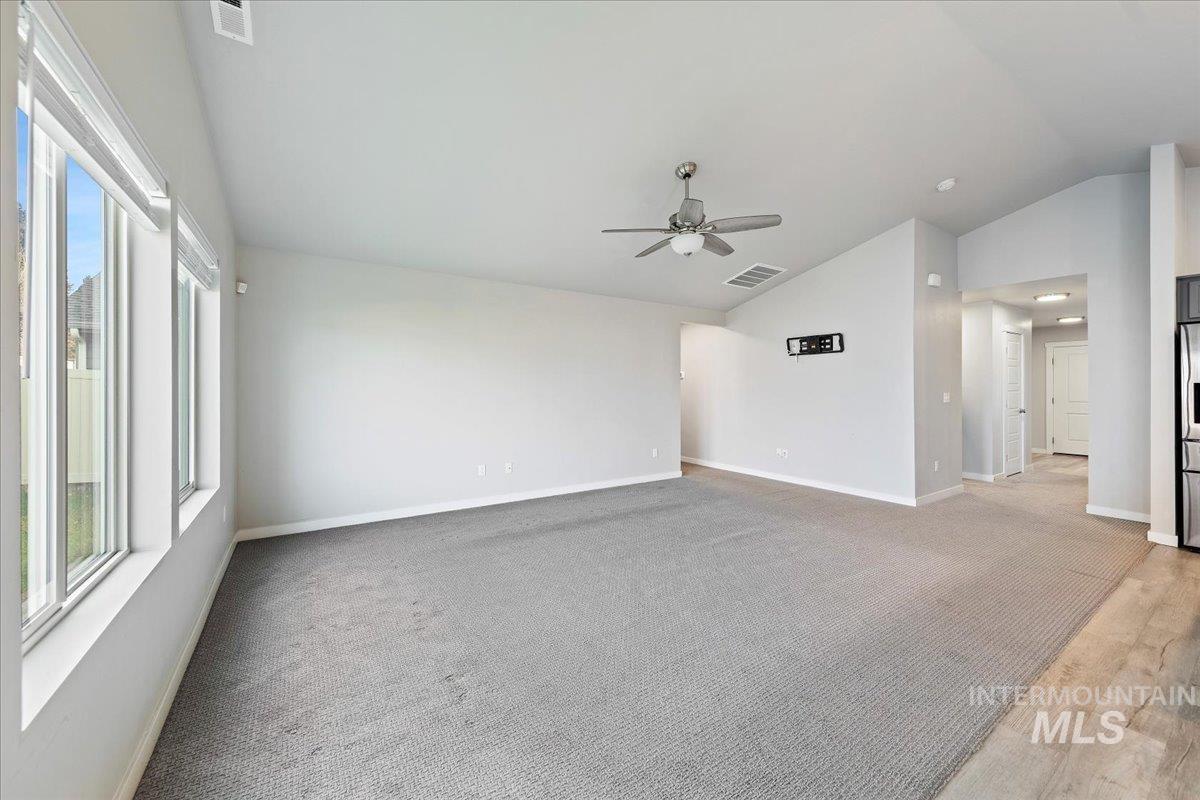 Spare room featuring light carpet, lofted ceiling, and a ceiling fan