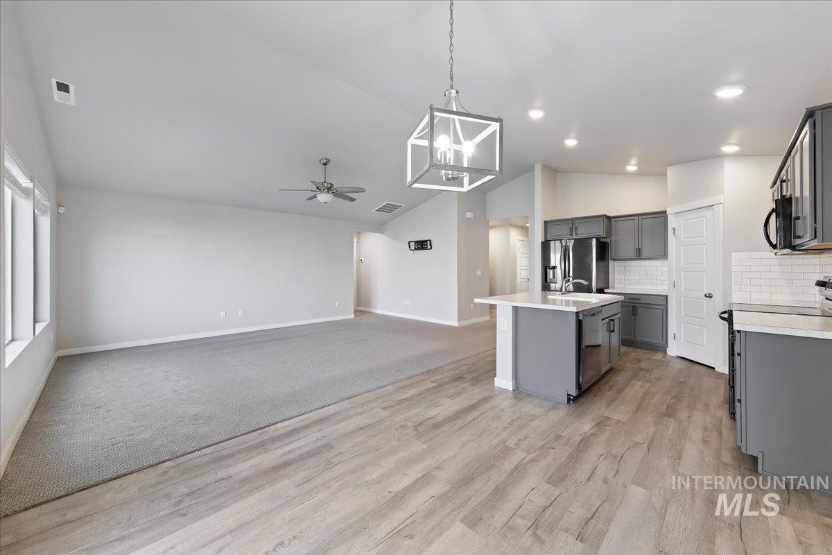 Kitchen with open floor plan, vaulted ceiling, appliances with stainless steel finishes, hanging light fixtures, and a kitchen island with sink