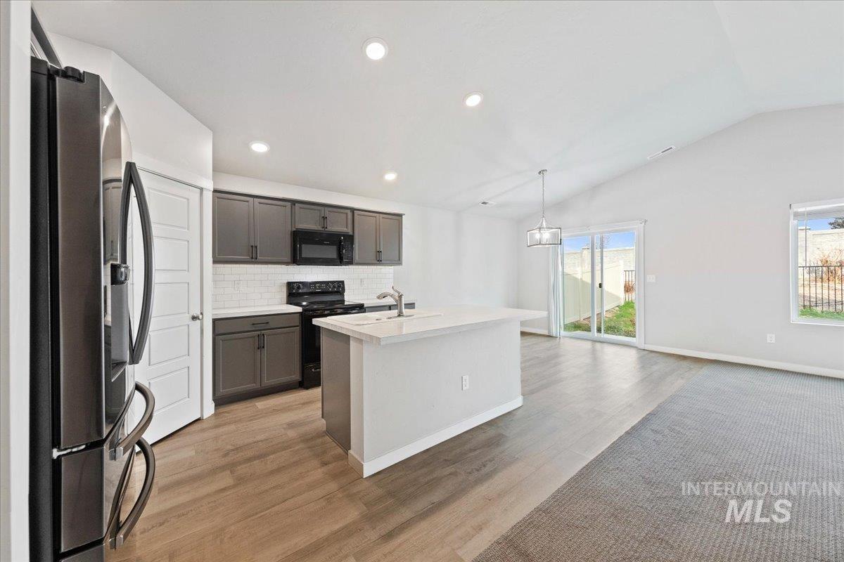 Kitchen featuring black appliances, a center island with sink, backsplash, light countertops, and pendant lighting