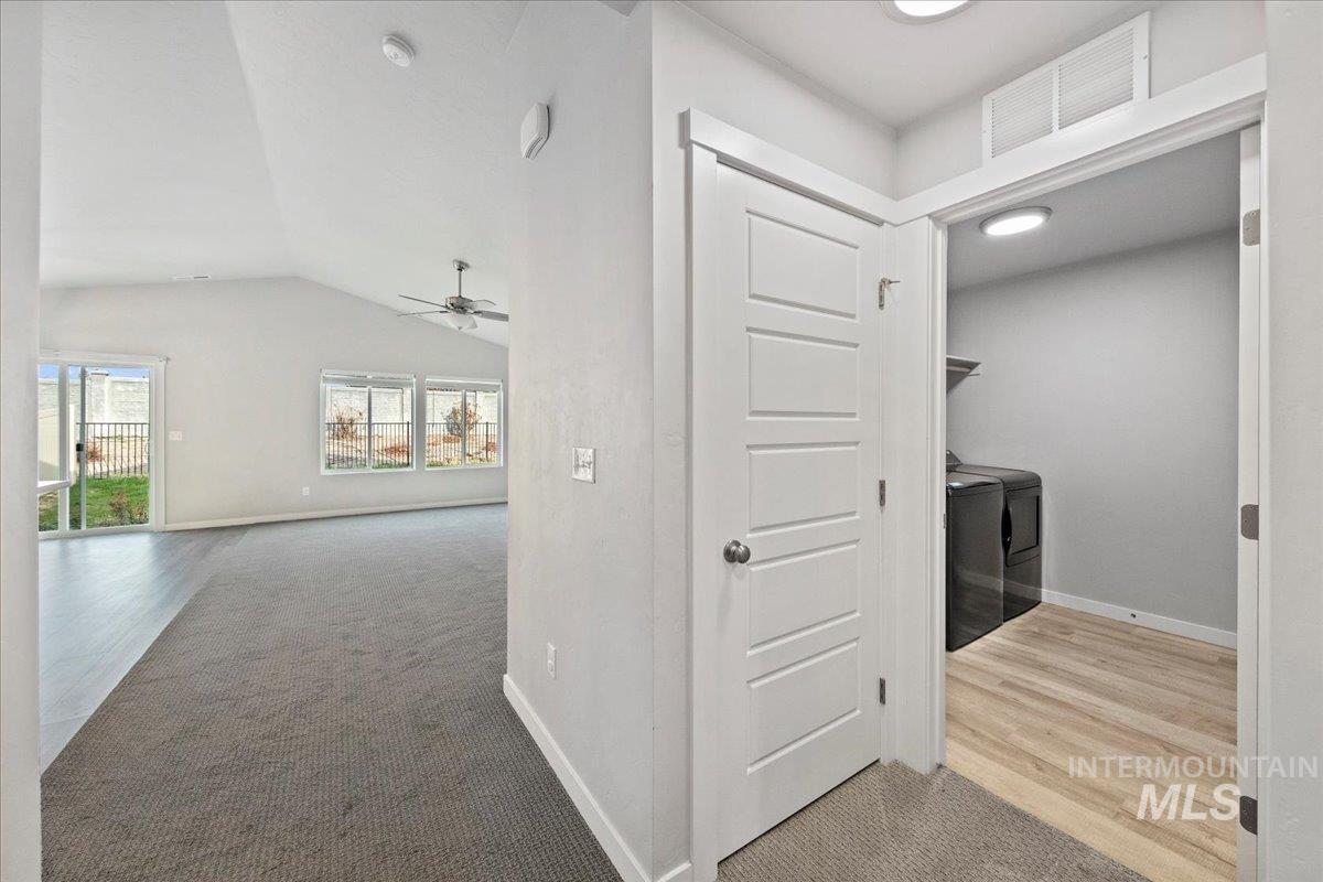 Hall featuring light colored carpet, light wood-type flooring, washing machine and clothes dryer, and lofted ceiling