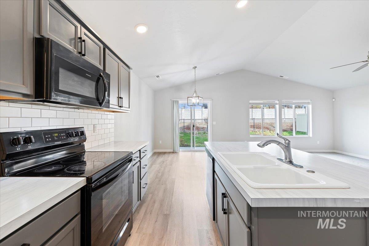 Kitchen with black appliances, gray cabinetry, light countertops, hanging light fixtures, and tasteful backsplash