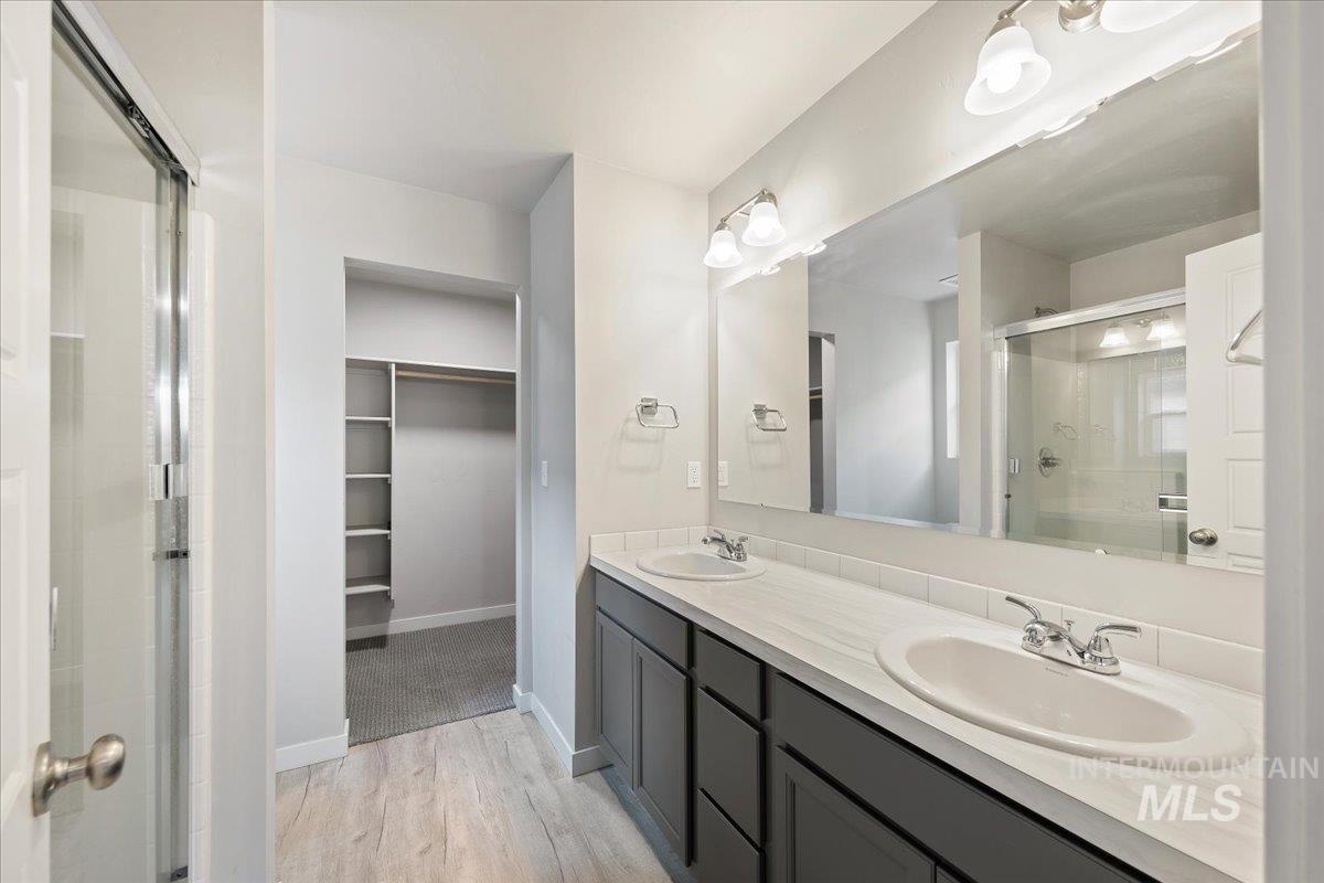 Full bath with a shower stall, double vanity, a walk in closet, and light wood-style flooring