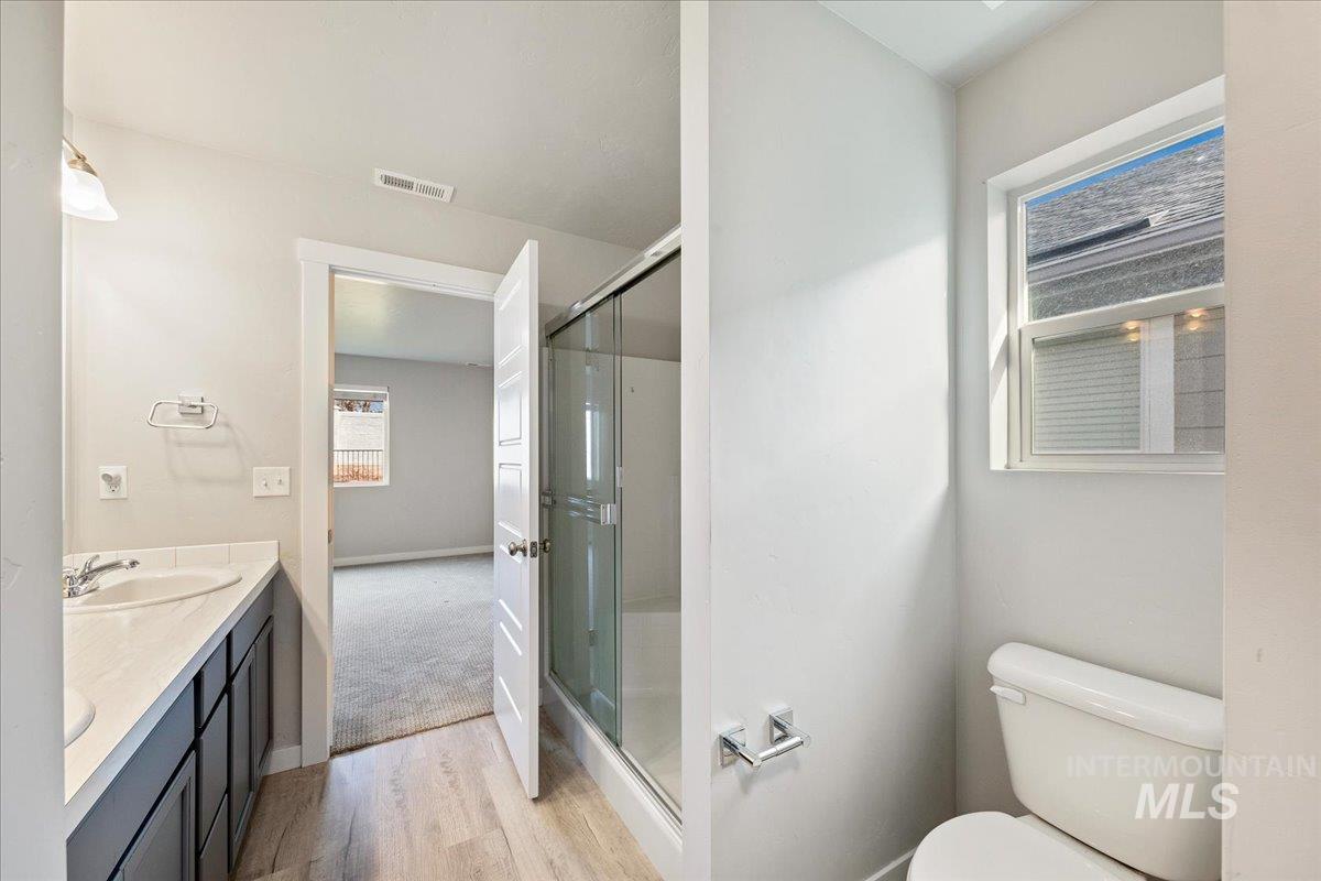 Full bath with double vanity, a stall shower, and light wood-type flooring