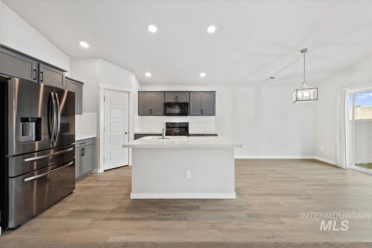 Kitchen with black appliances, decorative backsplash, hanging light fixtures, light wood-style floors, and recessed lighting