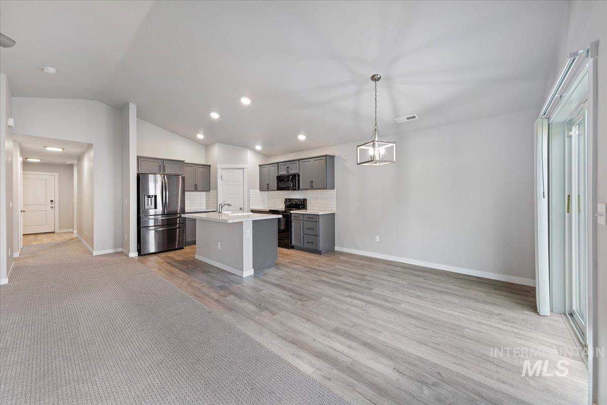 Kitchen with gray cabinetry, black appliances, lofted ceiling, open floor plan, and a center island with sink