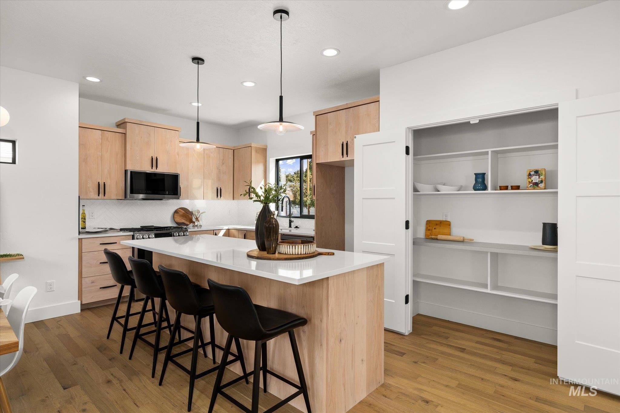 Kitchen featuring light brown cabinets, hanging light fixtures, a breakfast bar, a kitchen island, and dark wood-style floors