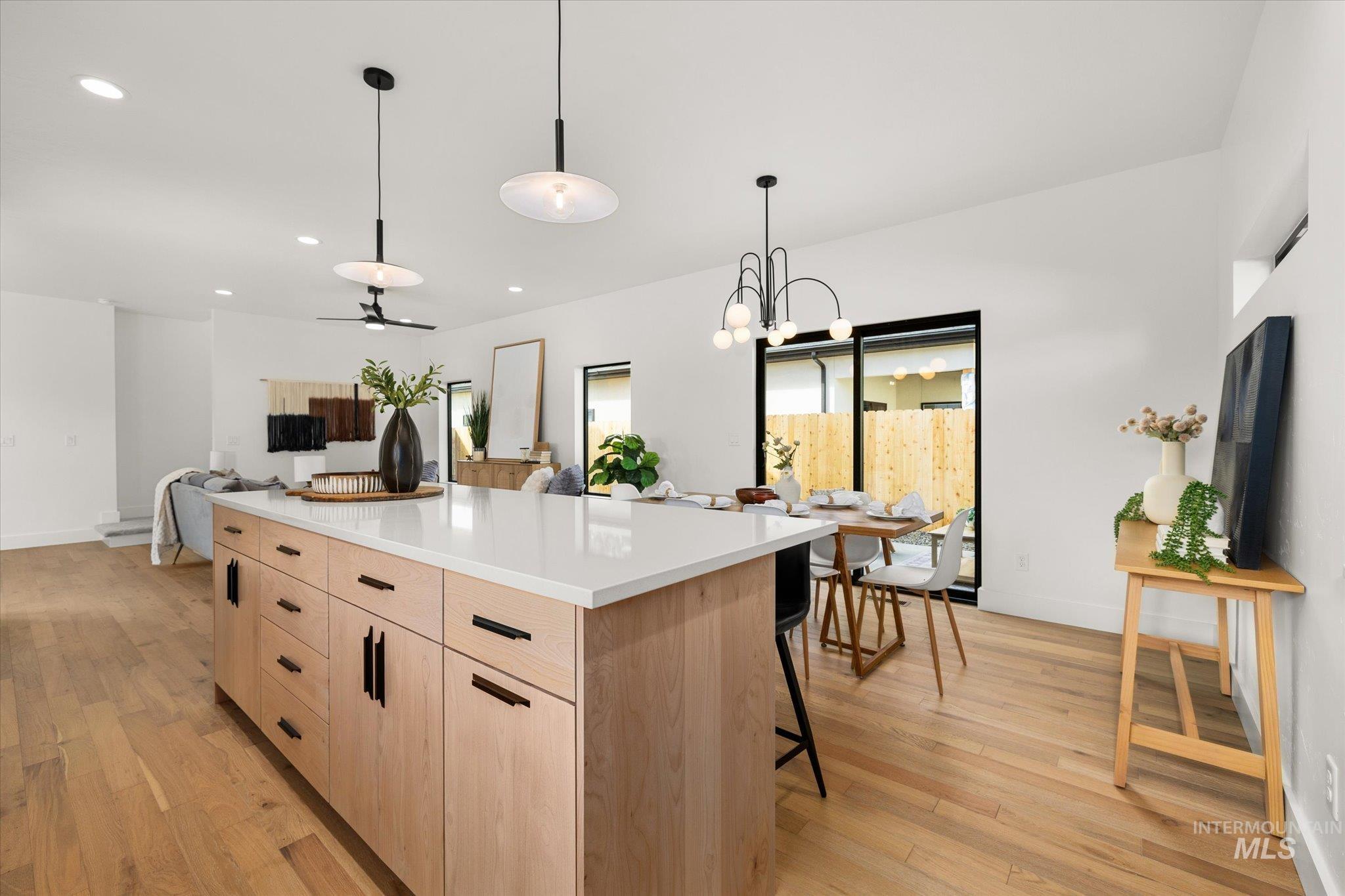 Kitchen with light brown cabinets, ceiling fan, a kitchen island, light wood-type flooring, and pendant lighting