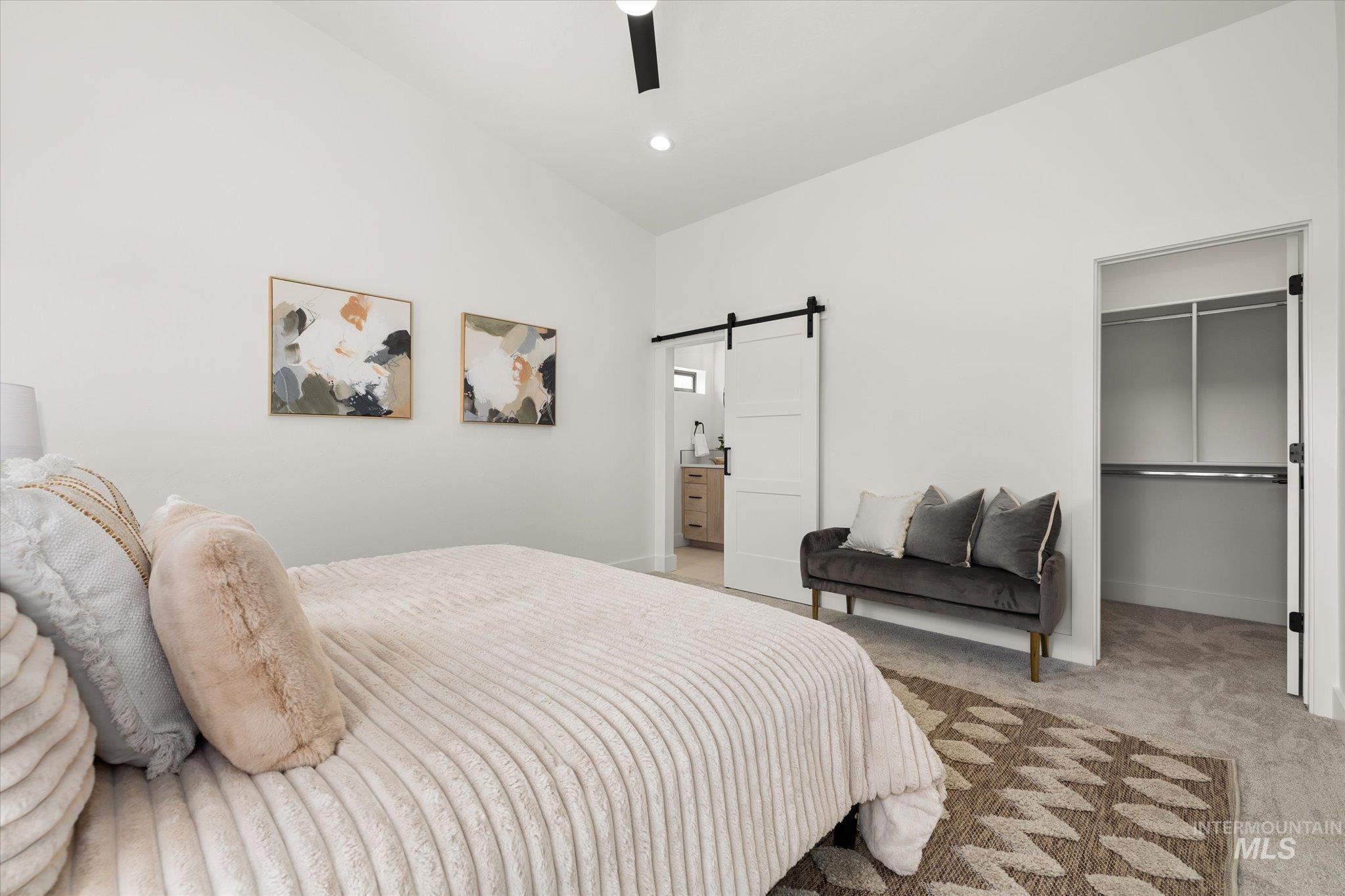 Bedroom featuring carpet flooring, a barn door, a spacious closet, ceiling fan, and lofted ceiling