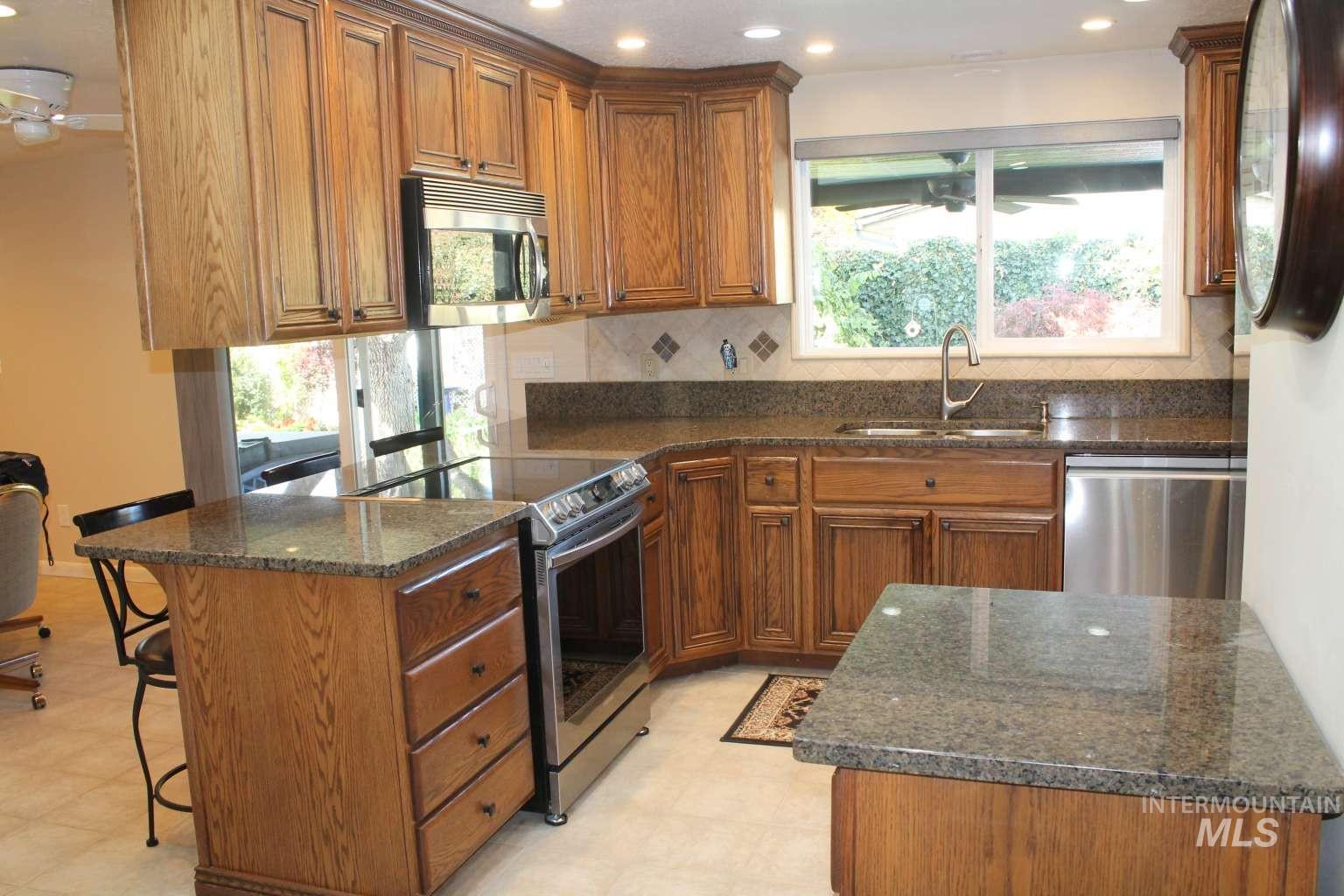Kitchen with brown cabinets, a peninsula, dark stone countertops, stainless steel appliances, and recessed lighting