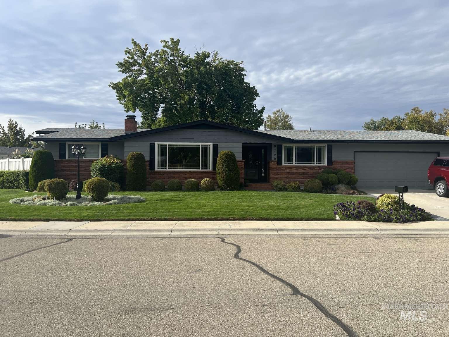 Ranch-style house featuring brick siding, a front lawn, an attached garage, concrete driveway, and a chimney