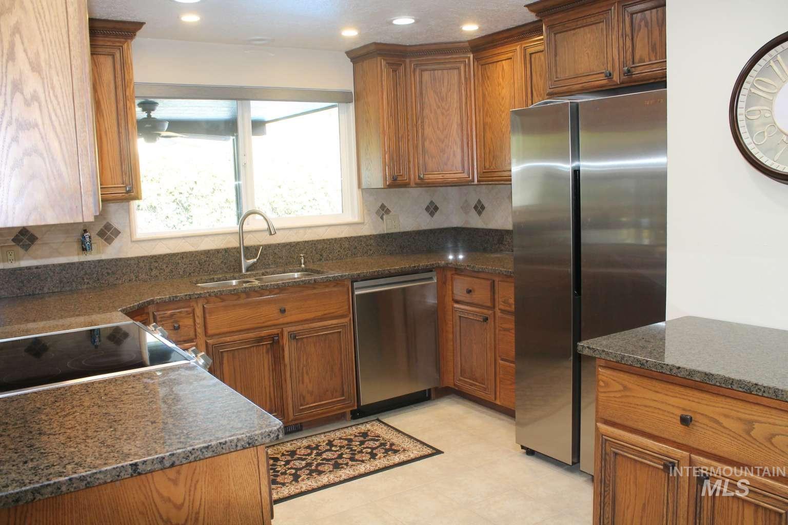 Kitchen with brown cabinetry, stainless steel appliances, tasteful backsplash, dark stone countertops, and recessed lighting