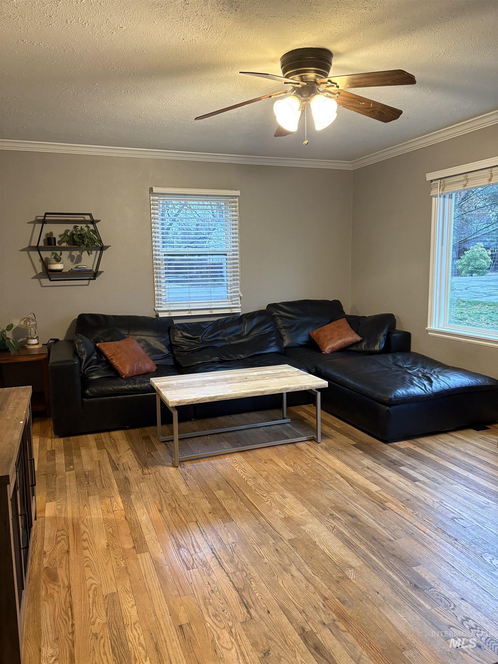Living area with light wood-type flooring, ornamental molding, a textured ceiling, and ceiling fan