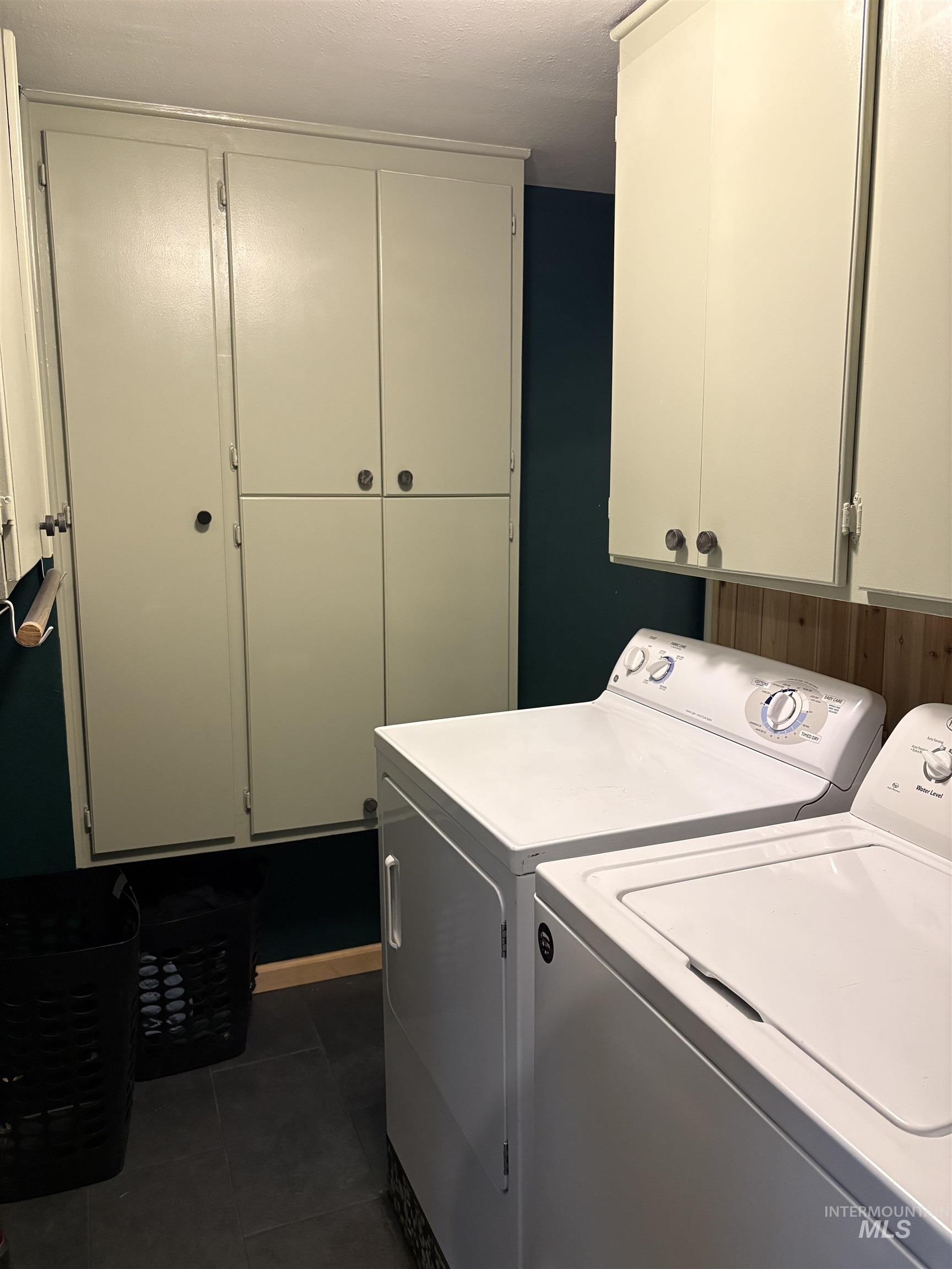 Laundry room with cabinet space, washer and clothes dryer, and dark tile patterned floors