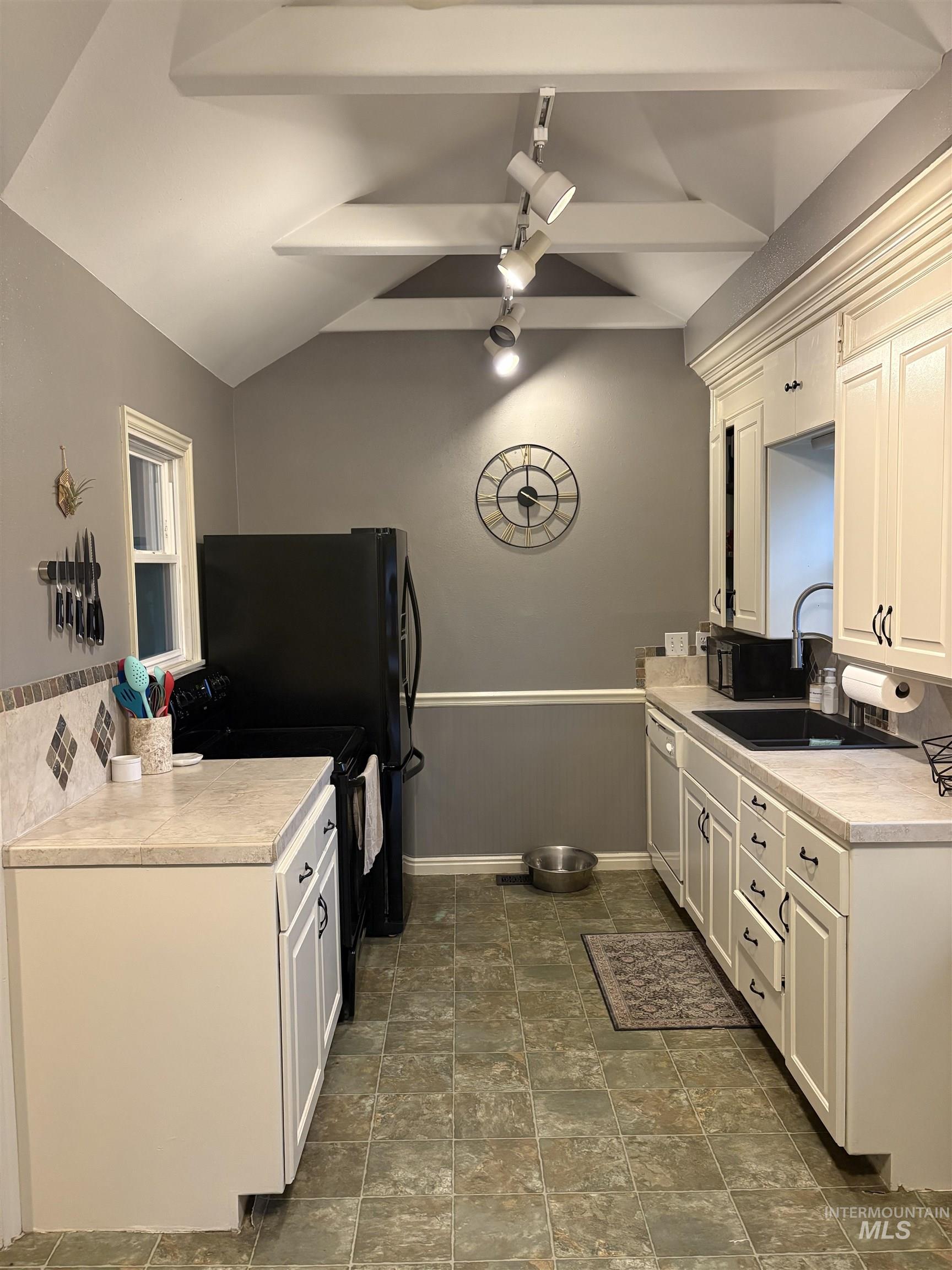 Kitchen featuring light countertops, backsplash, black range with electric stovetop, a wainscoted wall, and dishwashing machine