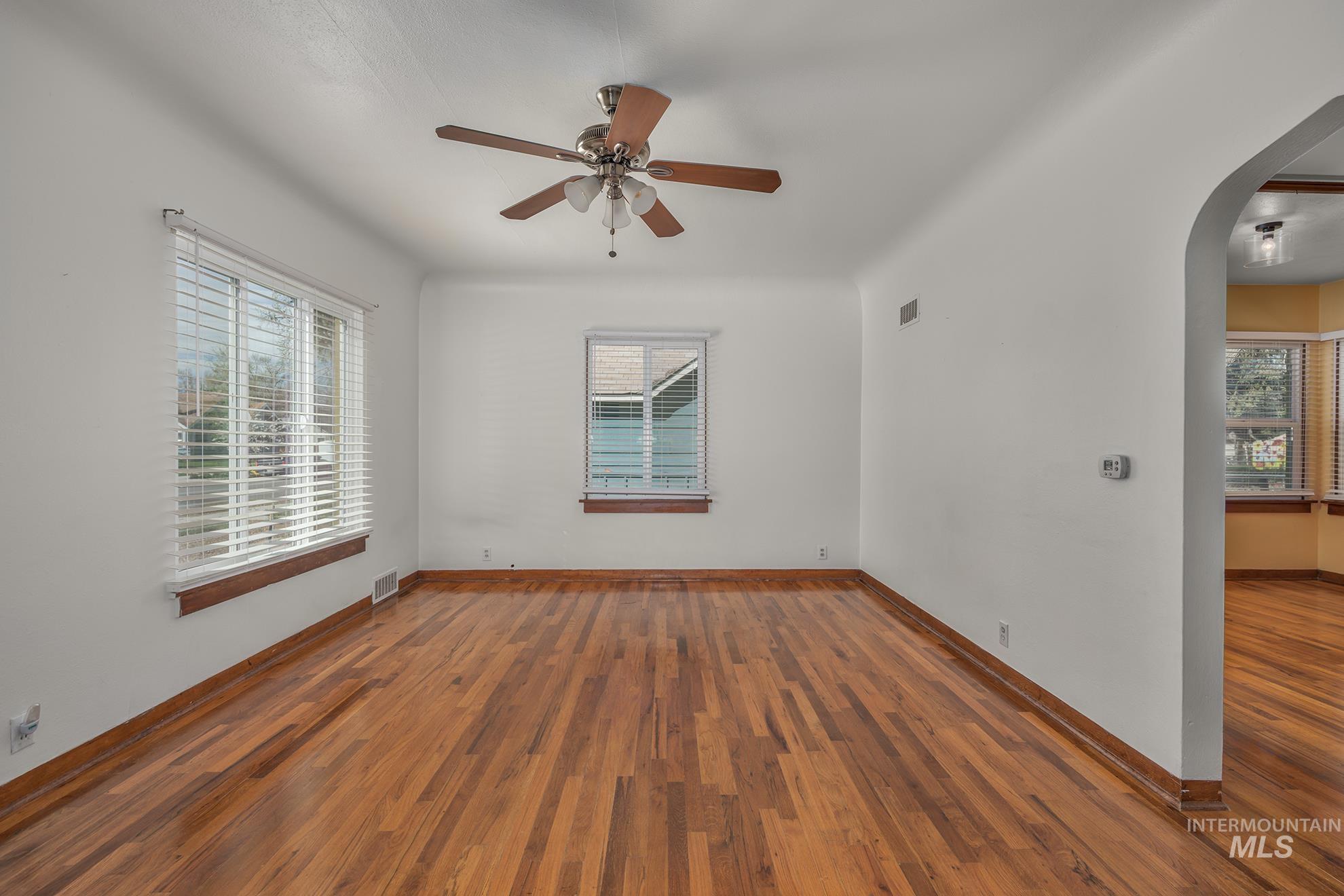 Empty room featuring arched walkways, wood-type flooring, and ceiling fan
