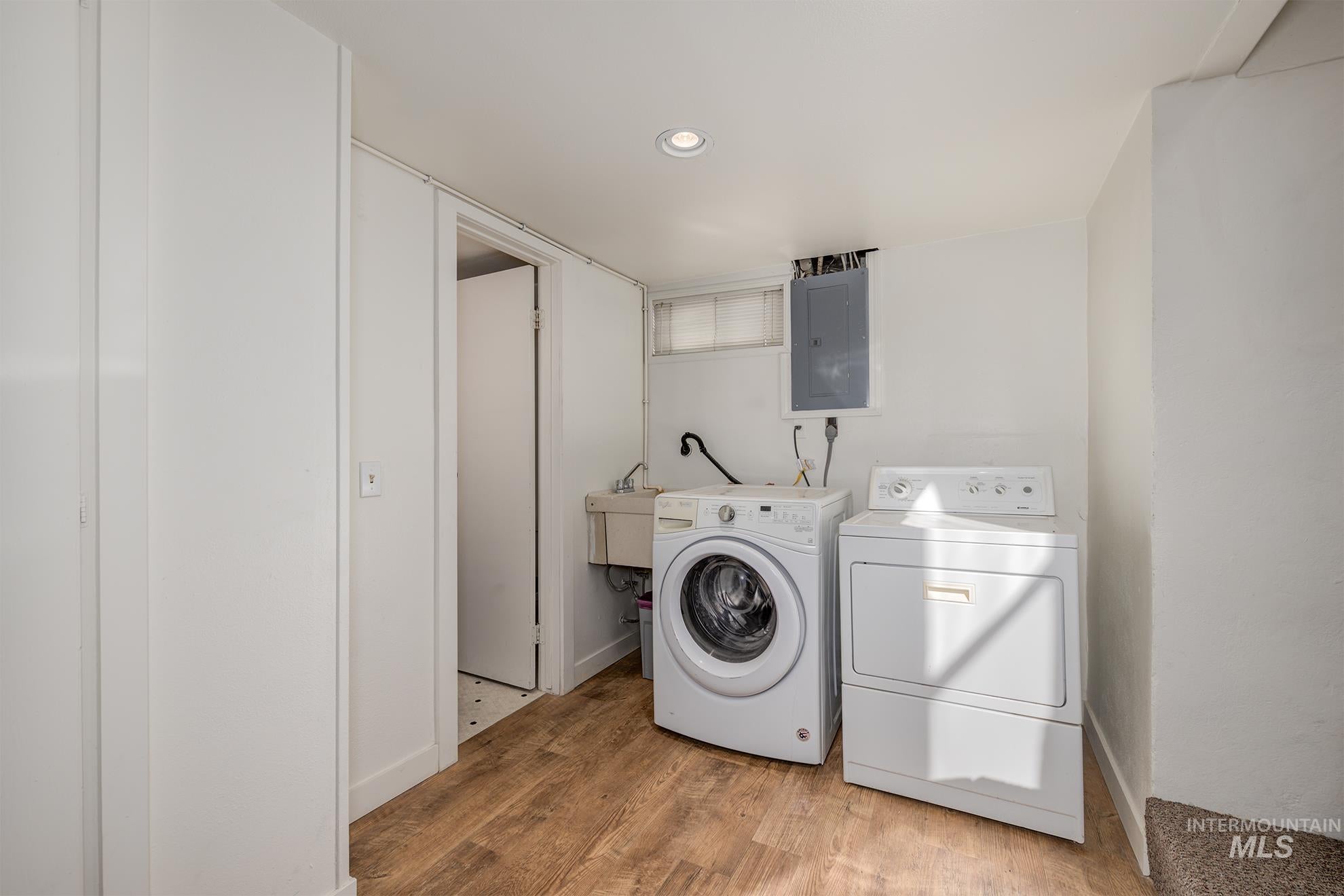 Laundry area with electric panel, light wood-style floors, washer and clothes dryer, and recessed lighting
