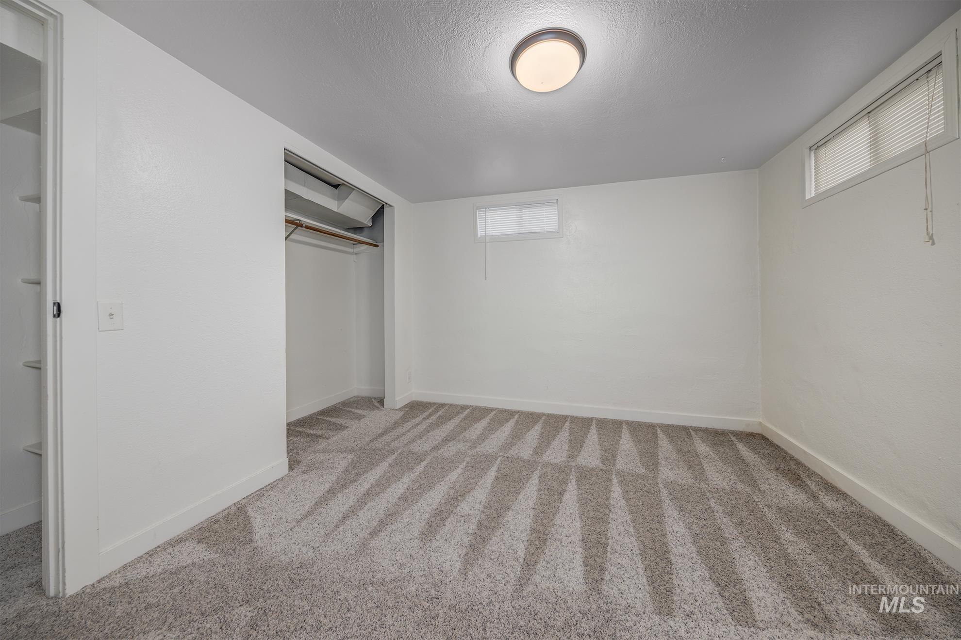 Unfurnished bedroom with a closet, light colored carpet, multiple windows, and a textured ceiling