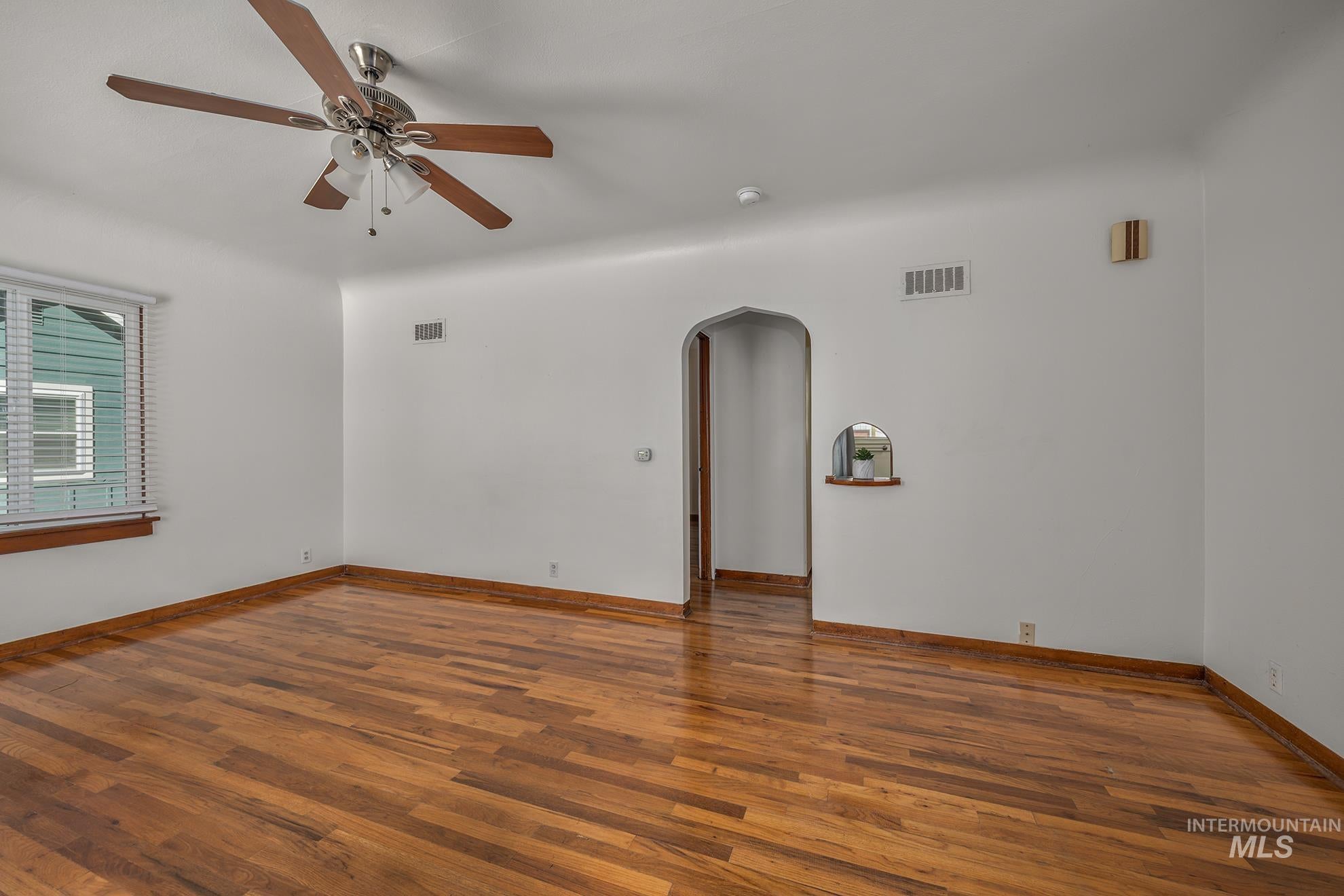 Unfurnished room featuring arched walkways, wood finished floors, and ceiling fan