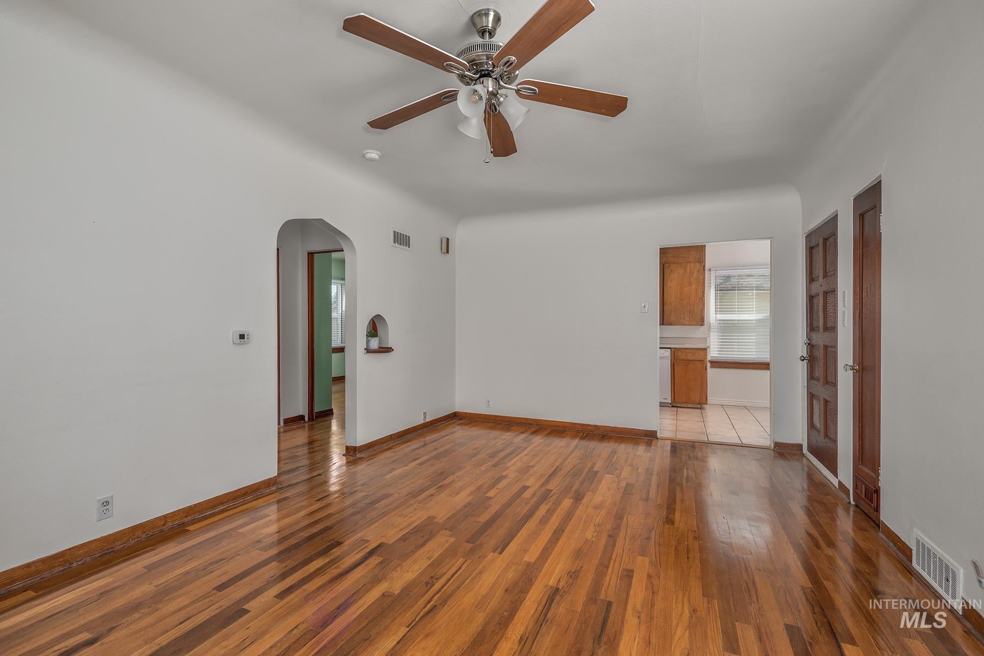 Unfurnished room featuring wood-type flooring, ceiling fan, and arched walkways