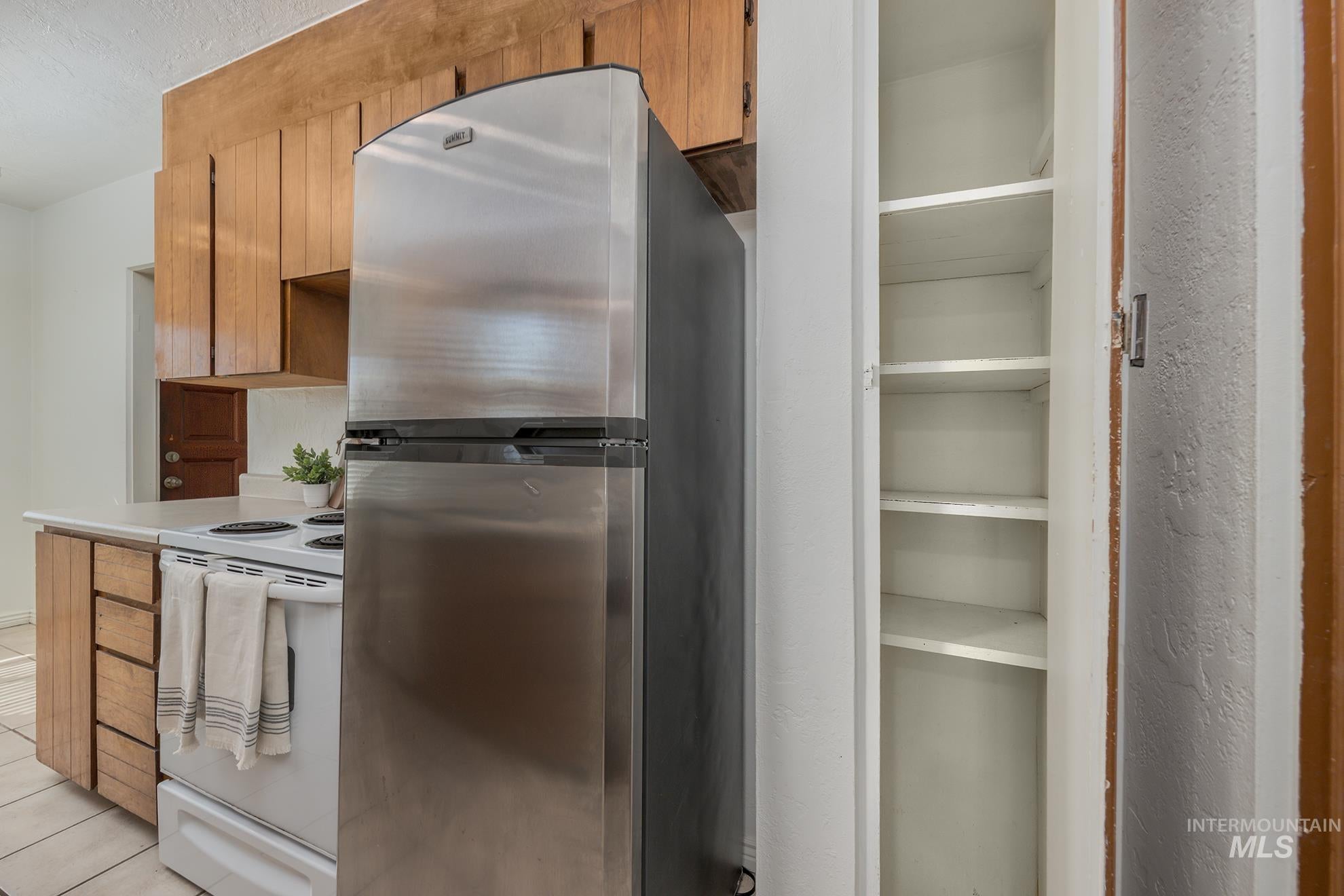 Kitchen featuring freestanding refrigerator, white range with electric cooktop, wood finish cabinets, and light countertops